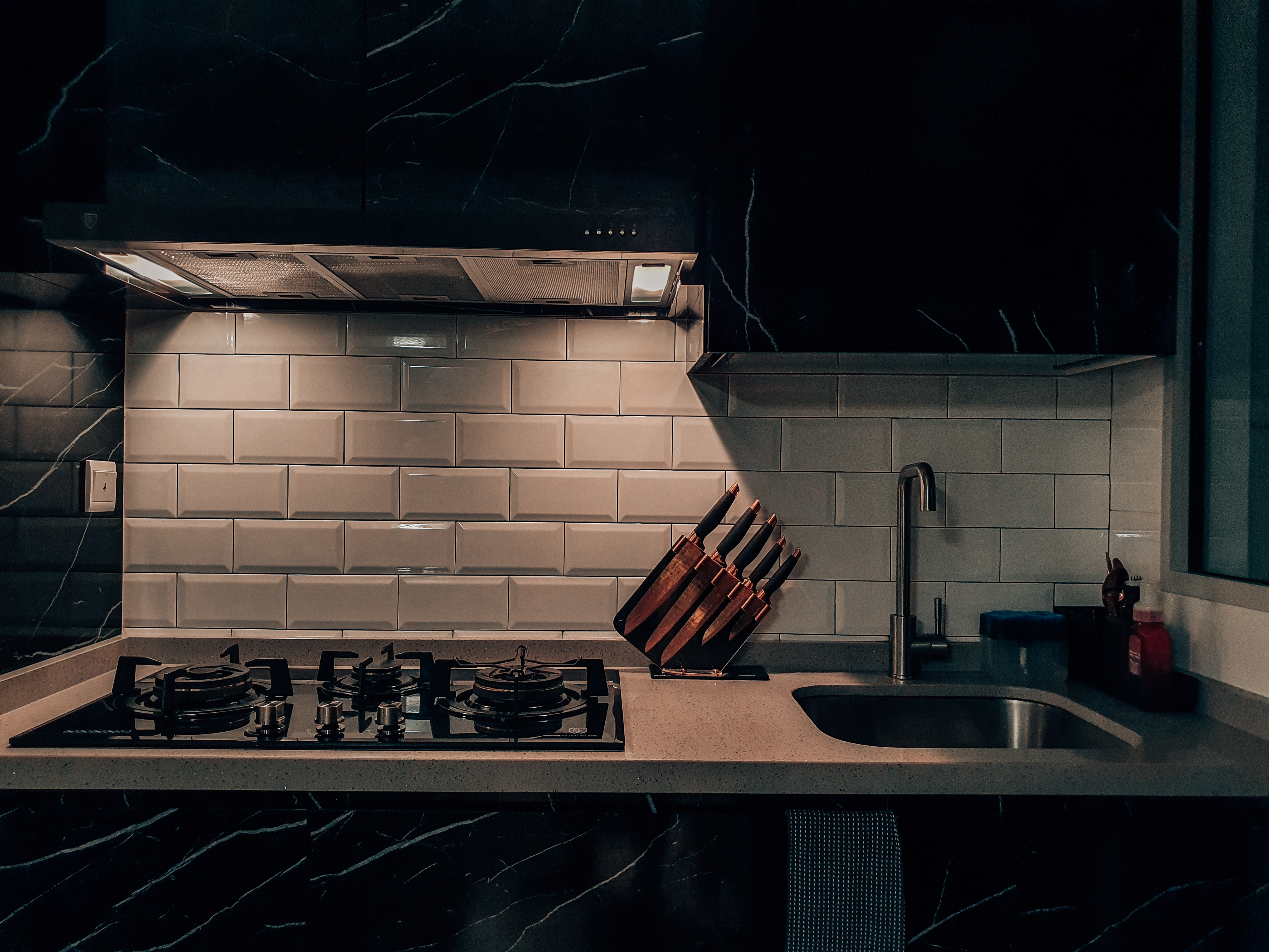 Atinymodernluxe dark kitchen - Dark marble kitchen, modern stove, black and white tiles, stainless steel range hood, knife