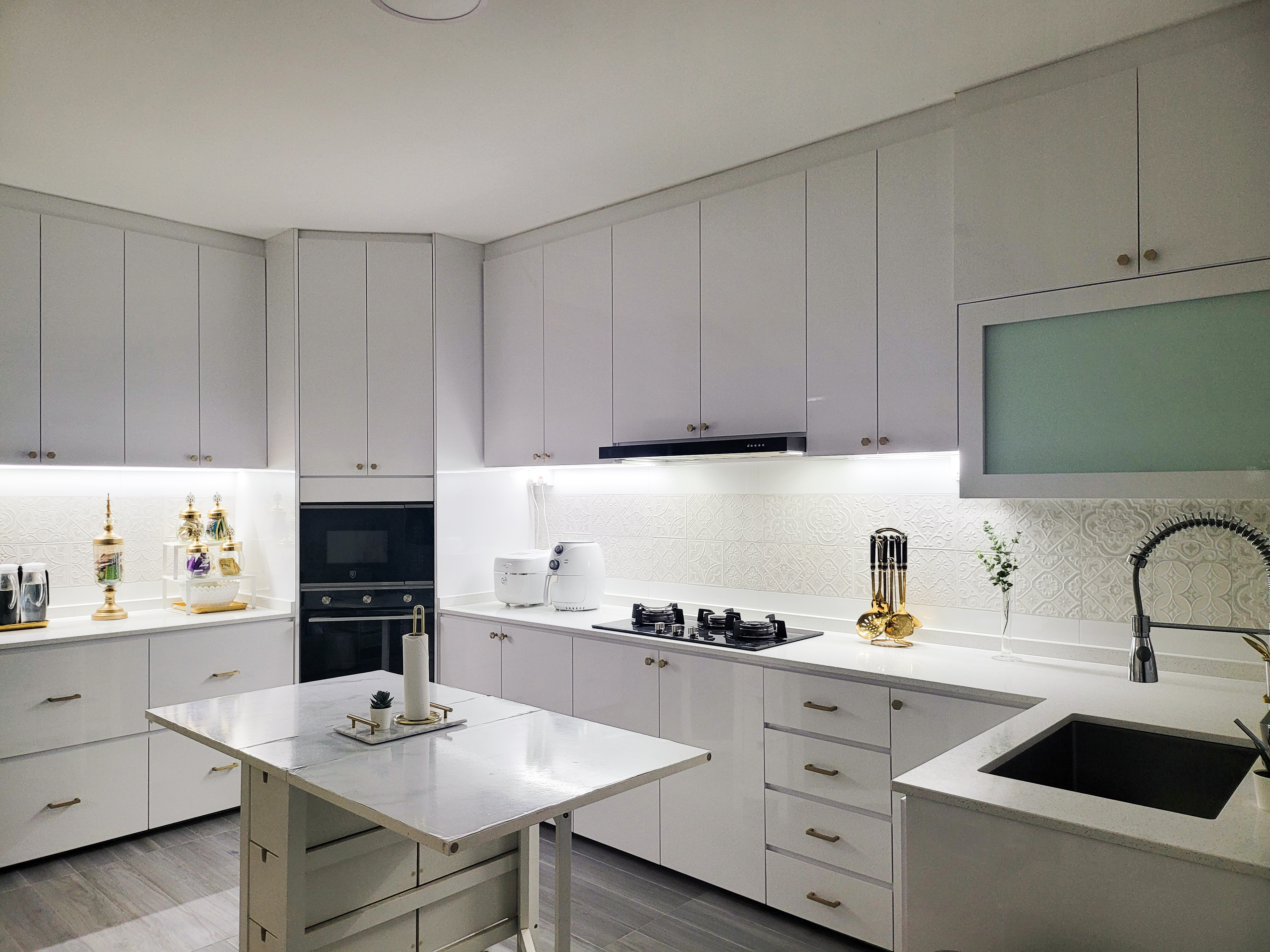Understated white Moroccan vibes - White kitchen cabinetry, modern appliances, black stovetop, white countertops, marble