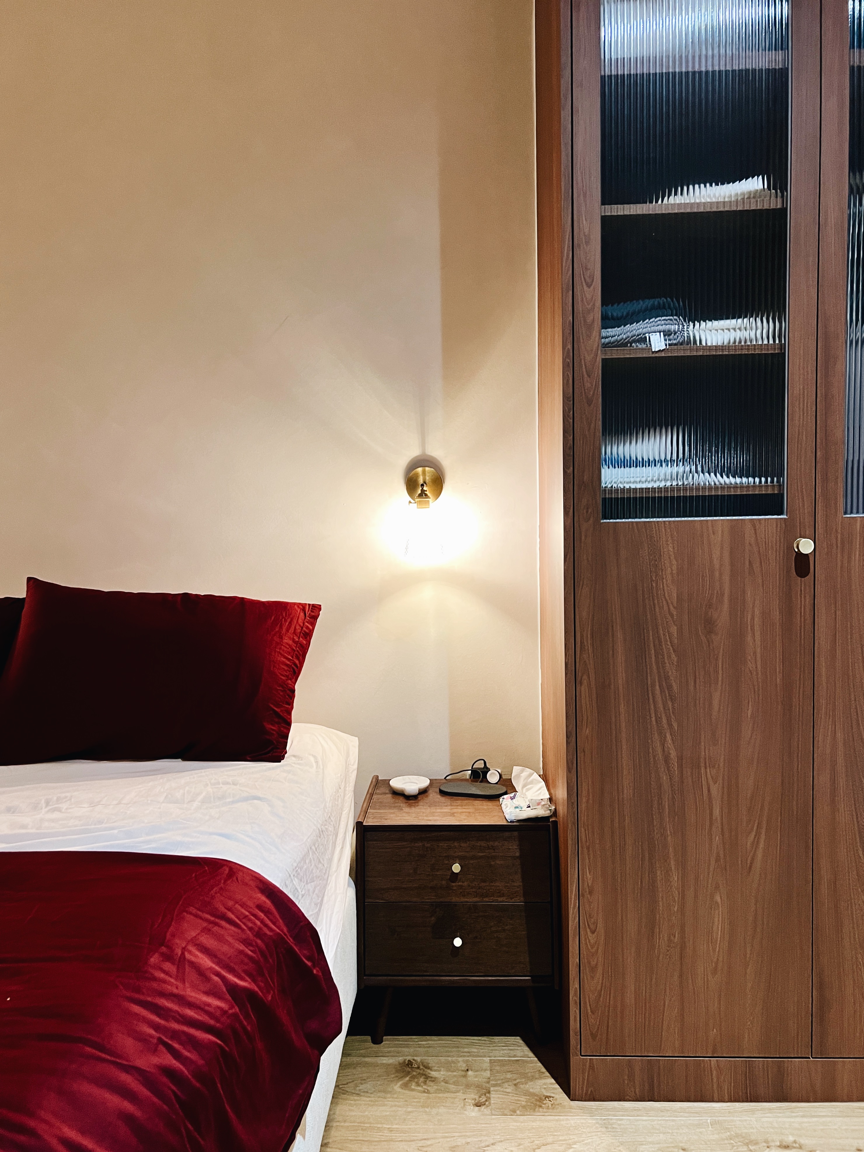 A cosy sanctuary to rest and recharge for the day ahead - Wooden nightstand, red pillows, white bedspread, bedside table