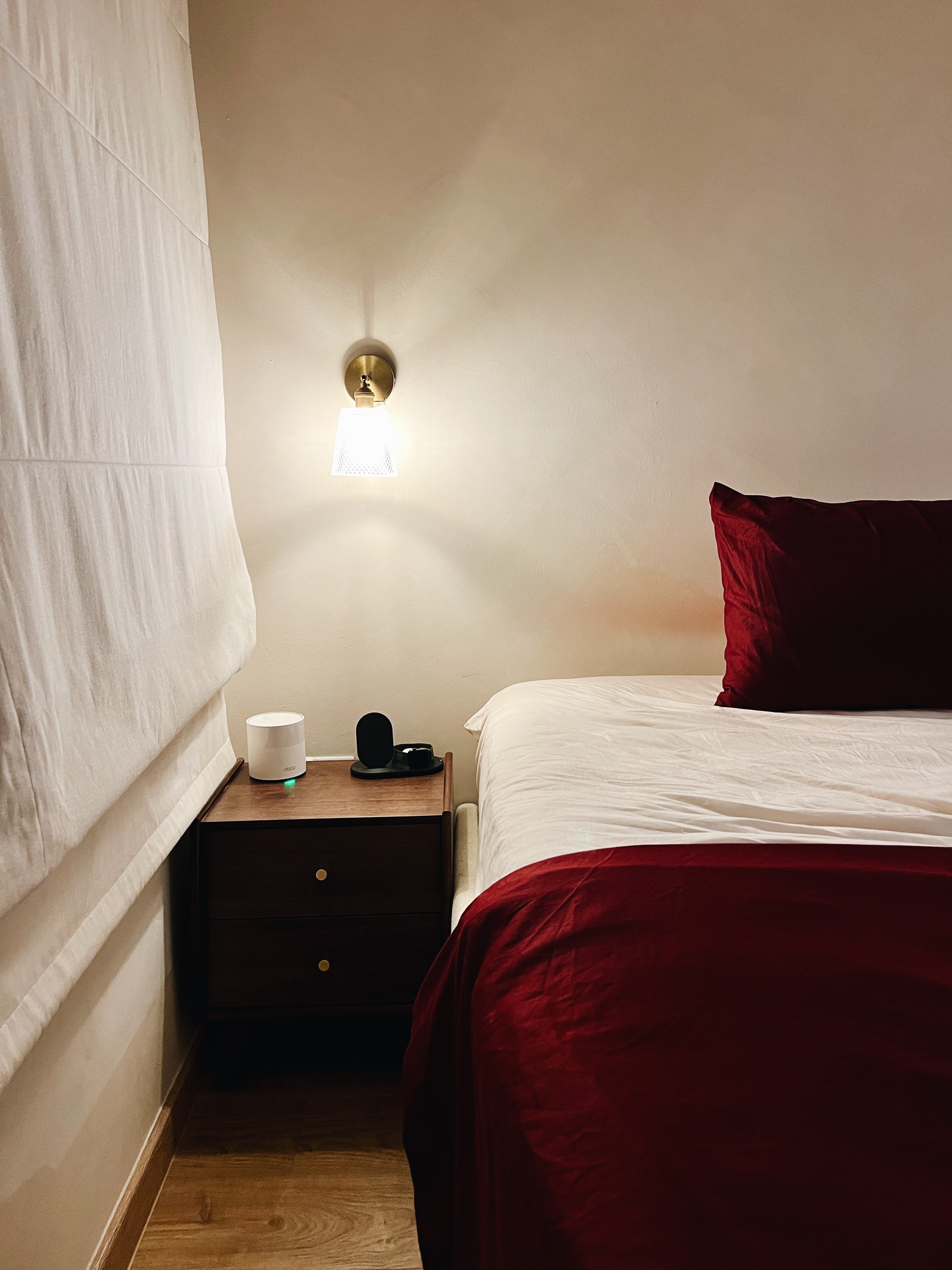 A cosy sanctuary to rest and recharge for the day ahead - White bed sheets, red pillows, wooden nightstand, wall-mounted