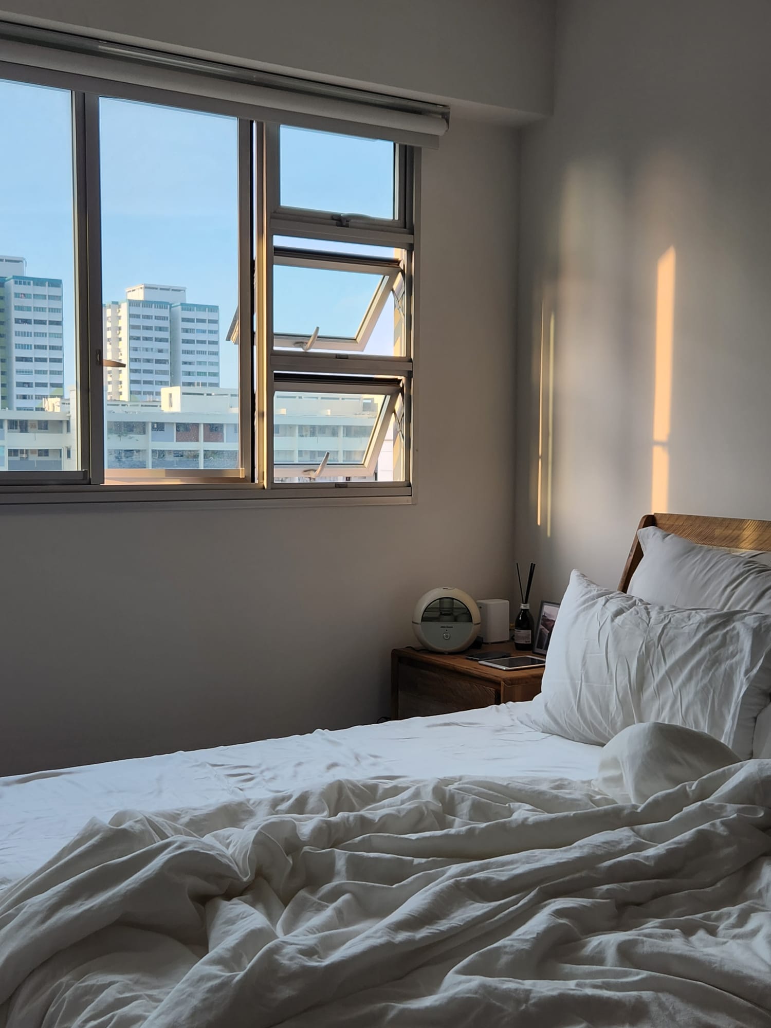 A warm and cozy bedroom to come home to - Sunlight streaming through window, cityscape view, modern bedroom, white bedding