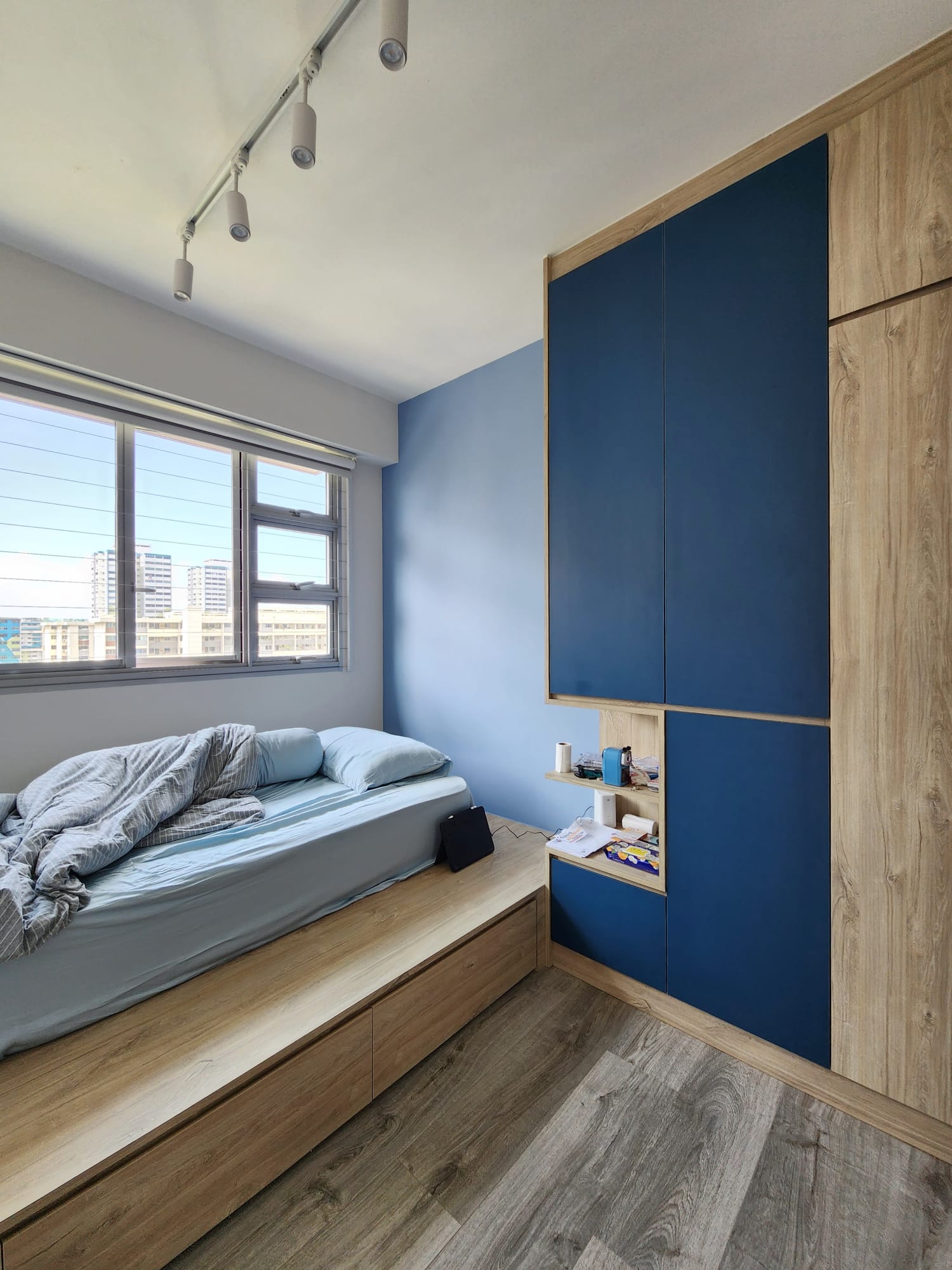 A warm and cozy bedroom to come home to - Modern bedroom with blue and wooden accents, large window with blinds, light blue