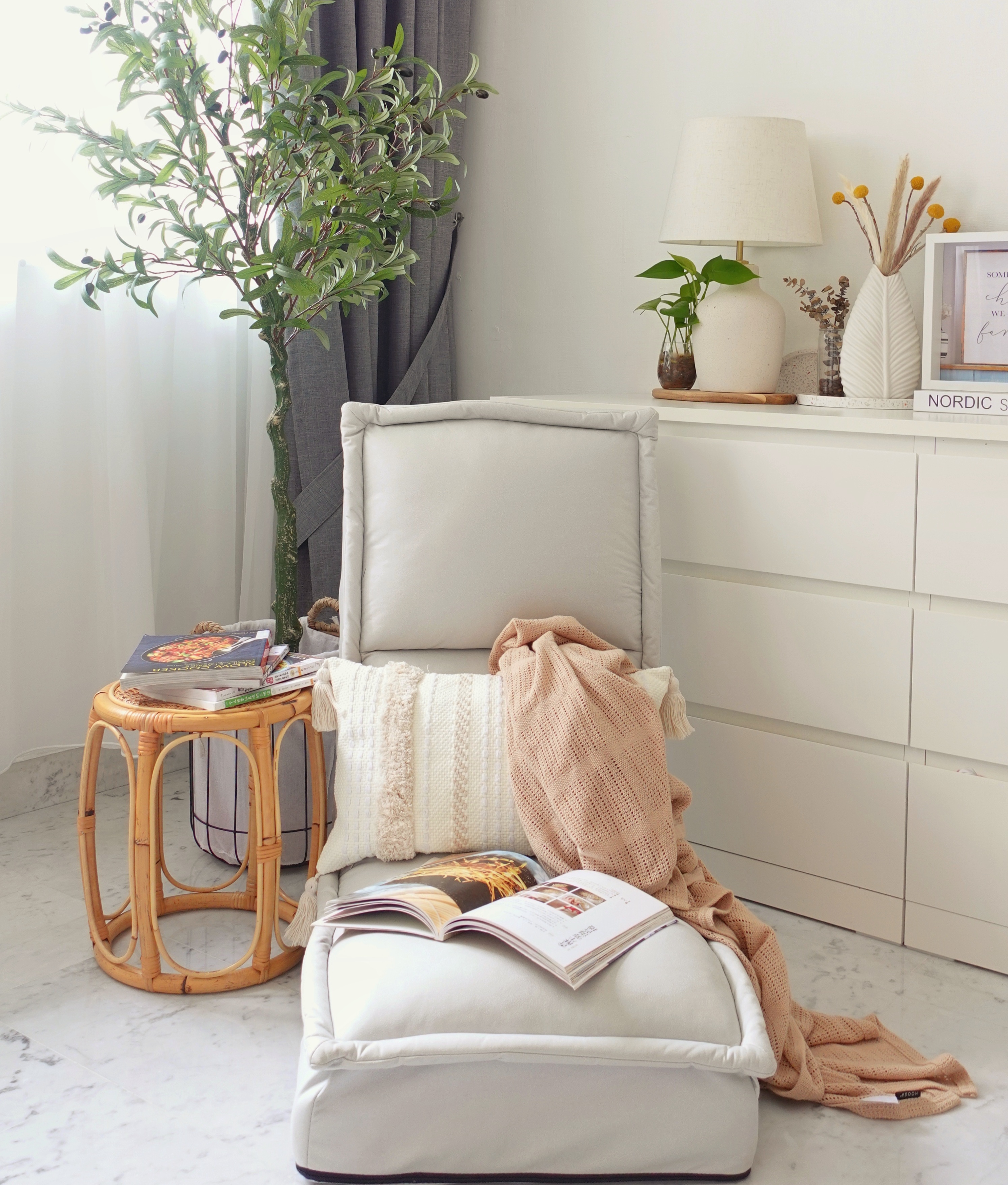 All Things Cosy In the Corners Of the Living Room - White cushion, cozy seating, soft pillows, beige blanket, open book