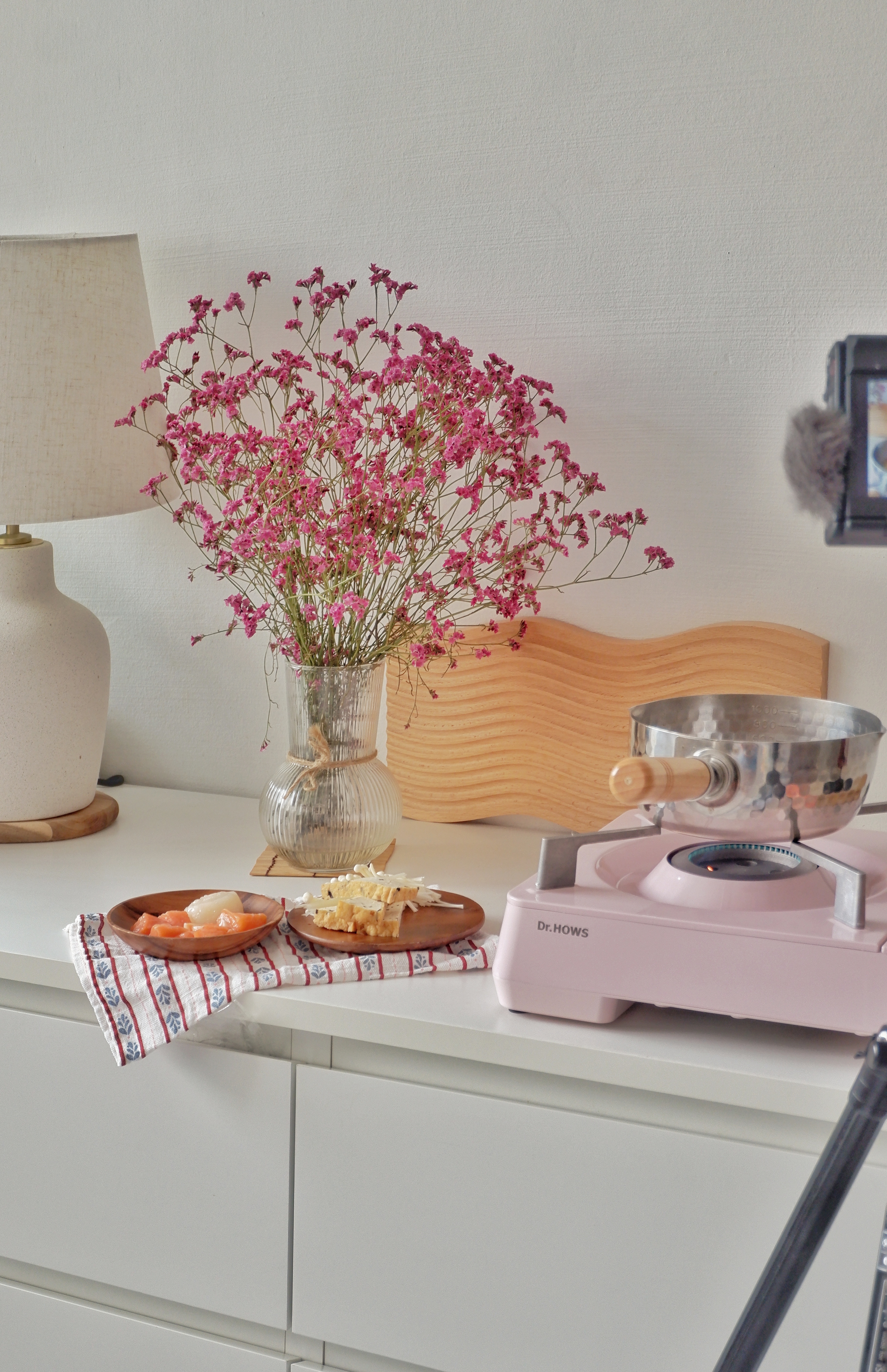All Things Cosy In the Corners Of the Living Room - vibrant pink flowers, white lamp, wooden cutting board, stainless steel
