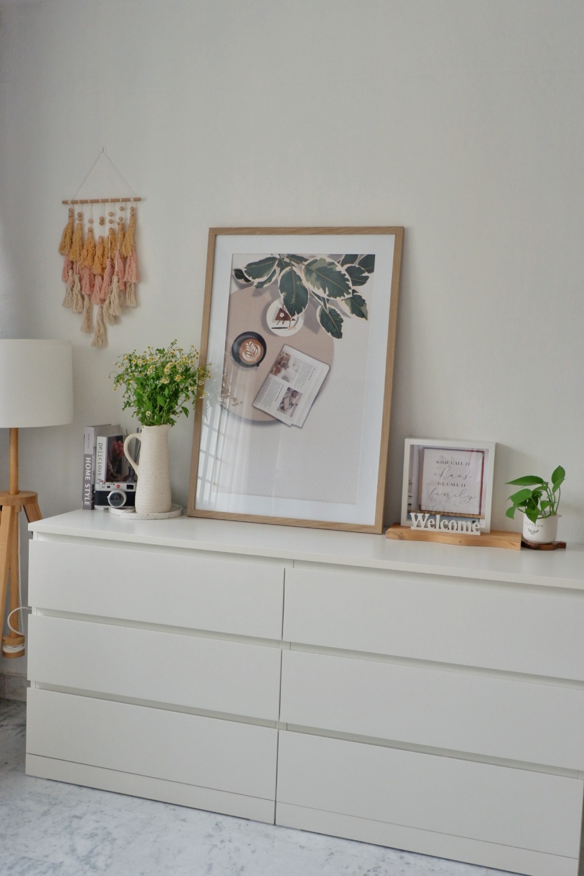 All Things Cosy In the Corners Of the Living Room - White dresser, minimalist decor, pastel wall art, wooden shelf, potted