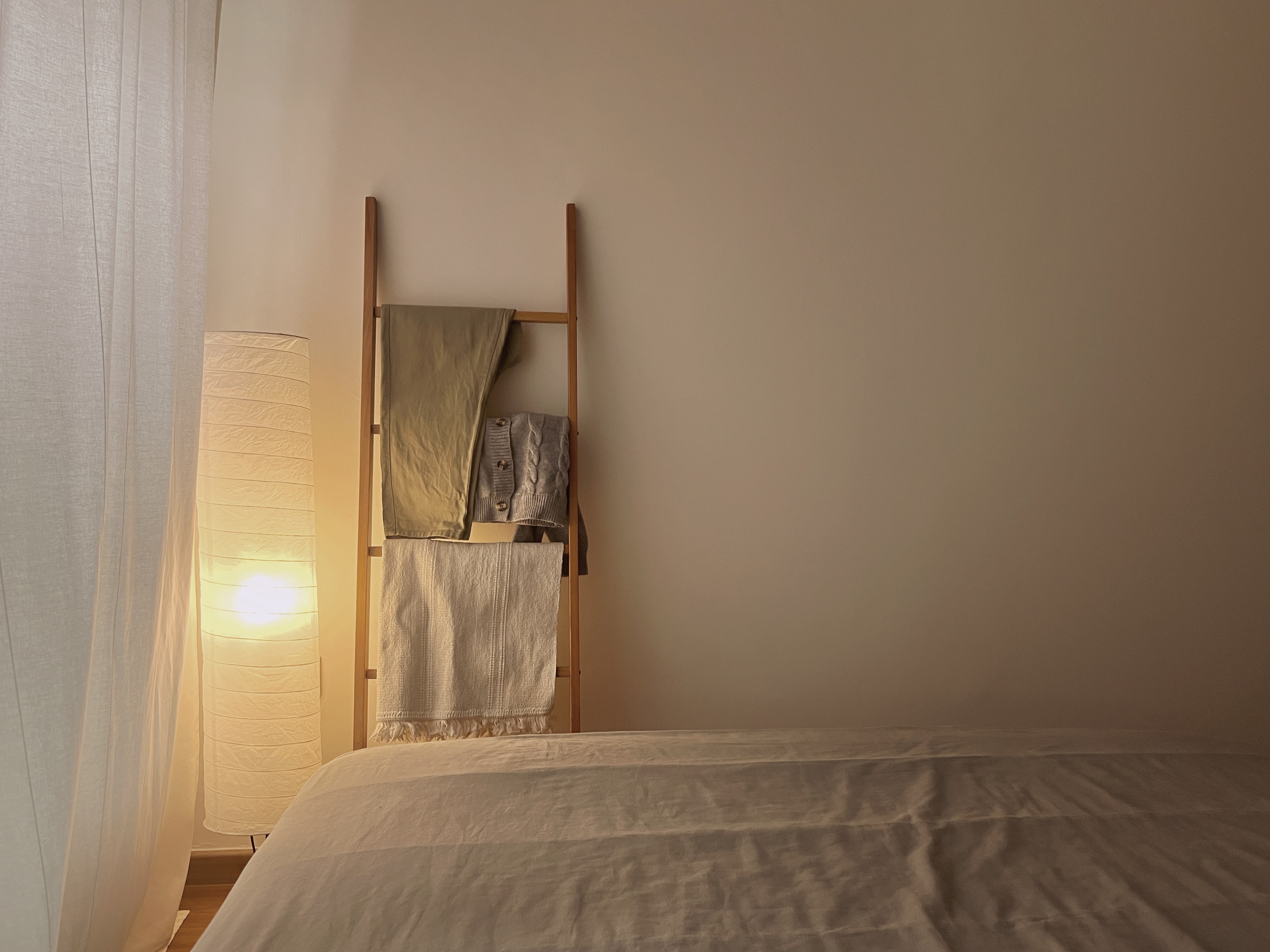Comfort without clutter - Lagom in the bedroom - Warm, cozy bedroom, soft lighting, wooden bed frame, neatly folded towels