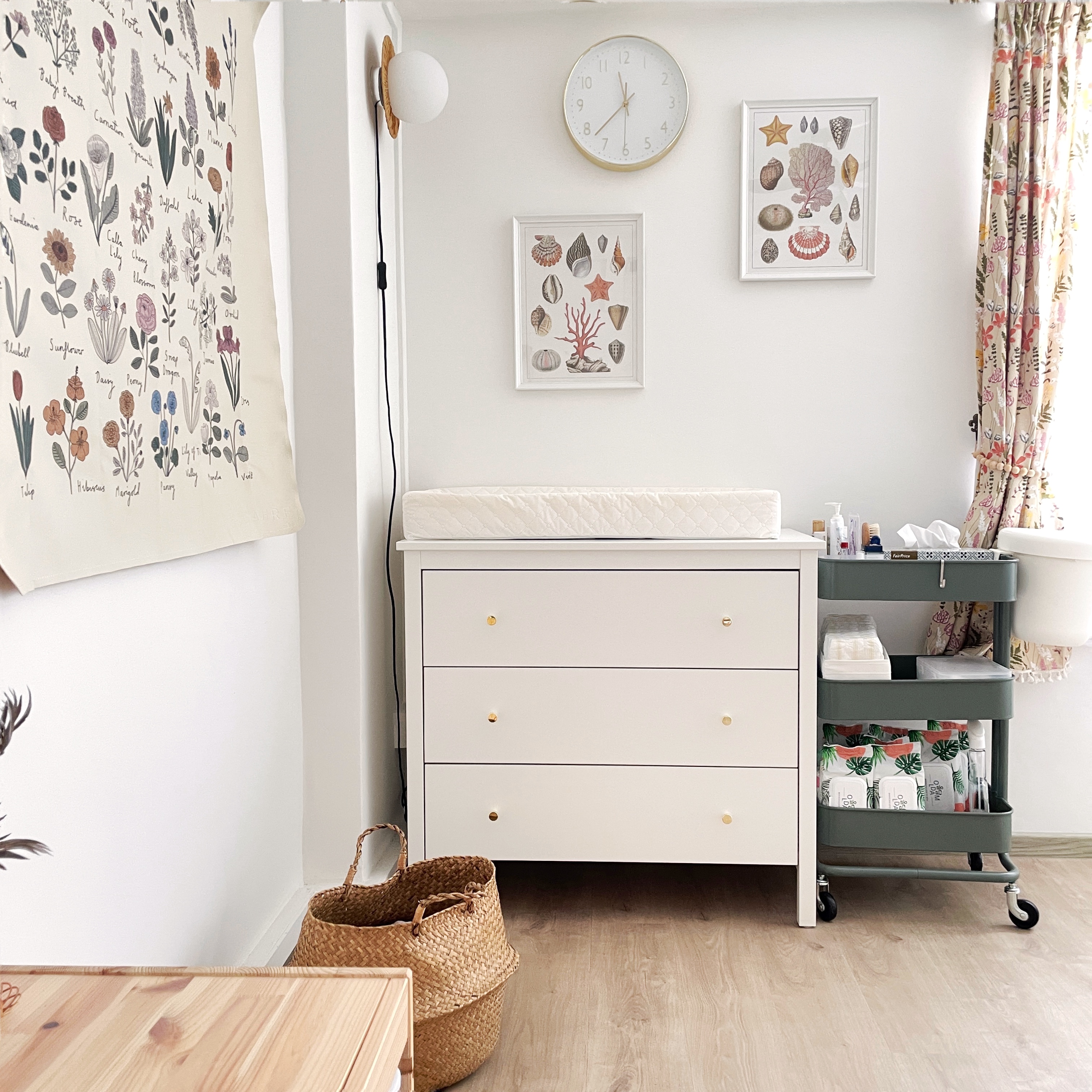 Calming and cheery nursery - White dresser with gold handles, neatly organized storage, floral wall art, clock above dresser