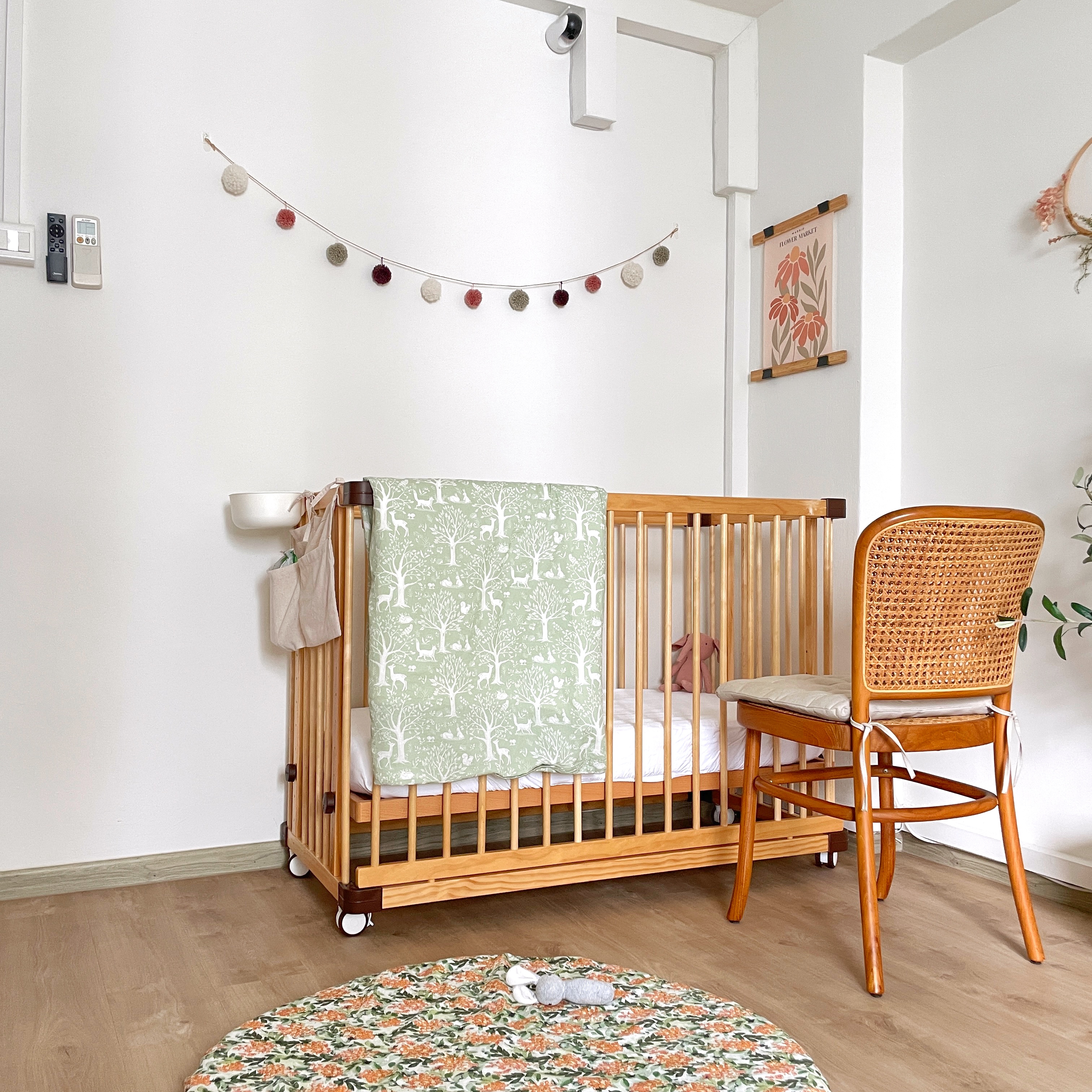 Calming and cheery nursery - Baby crib with green blanket, wooden crib frame, white wall decoration, baby chair, floral rug