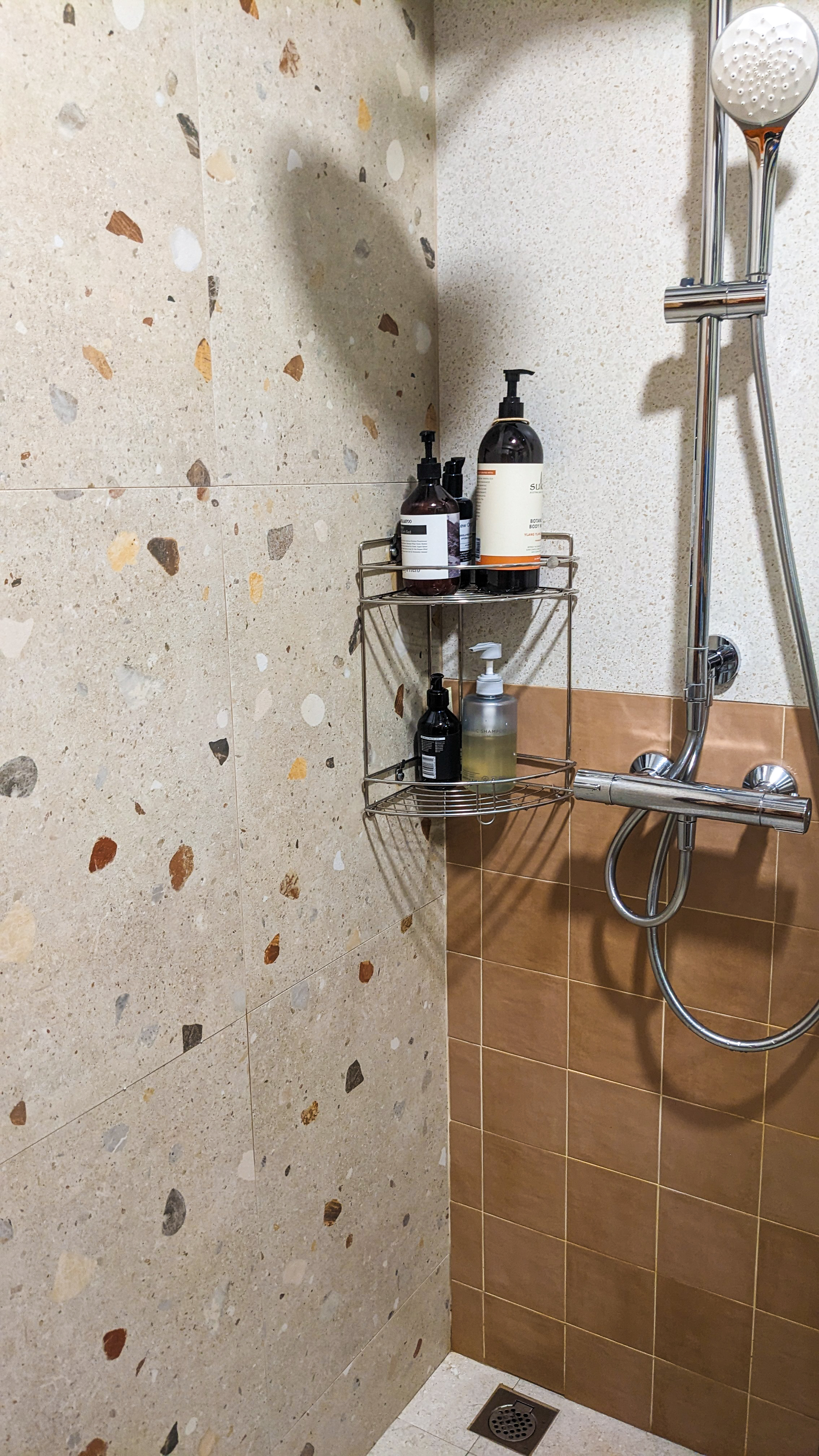 A Safe Haven | Skip to our Loo - Bathroom wall tiles with speckled patterns, metallic shower rack with toiletries, textured