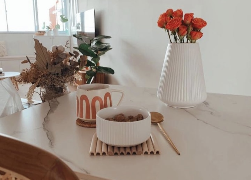 Where conversation happens - vibrant orange flowers, rustic ceramic mug, white textured vase, cozy indoor setting, natural