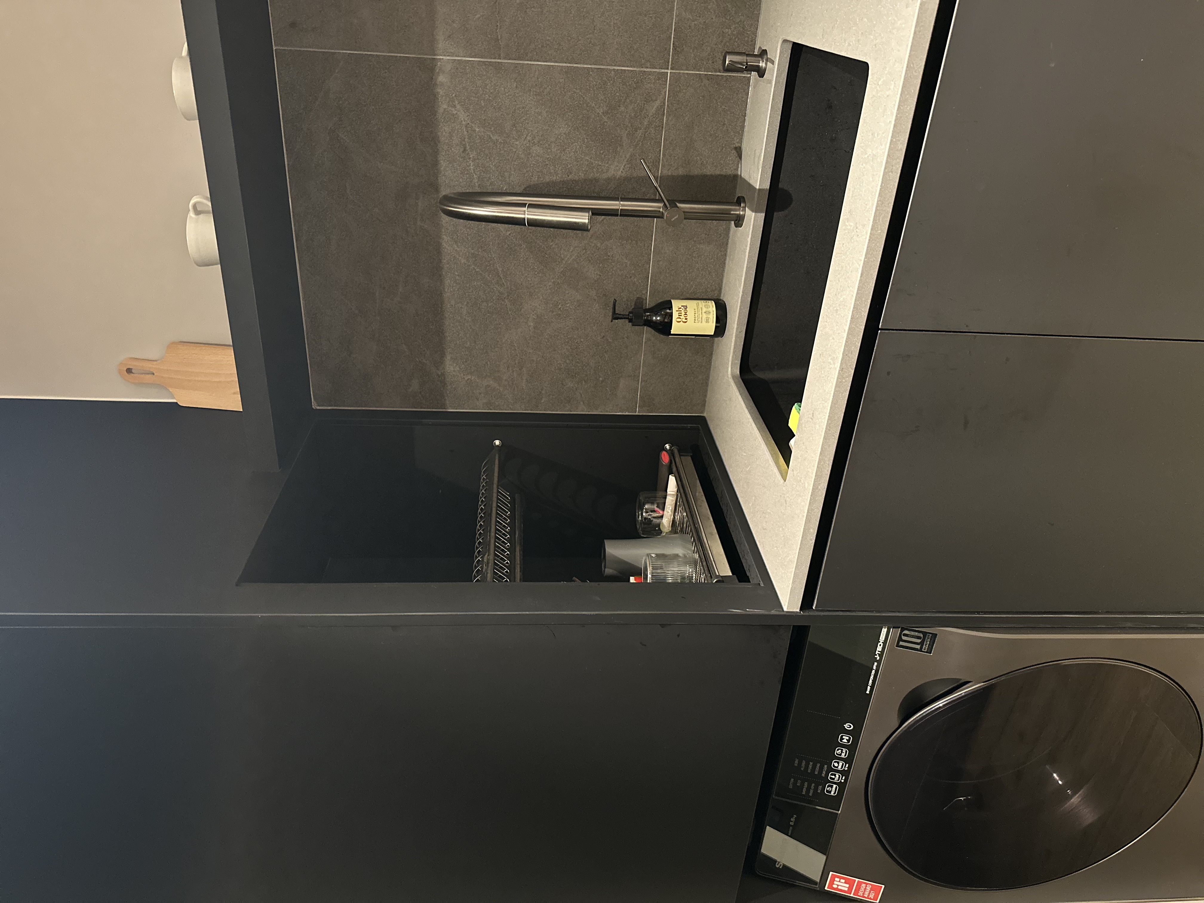 A modern dark themed kitchen  - microwave, kitchen, cabinets, countertop, sink, dish rack, wine bottle, wine glasses, cutting