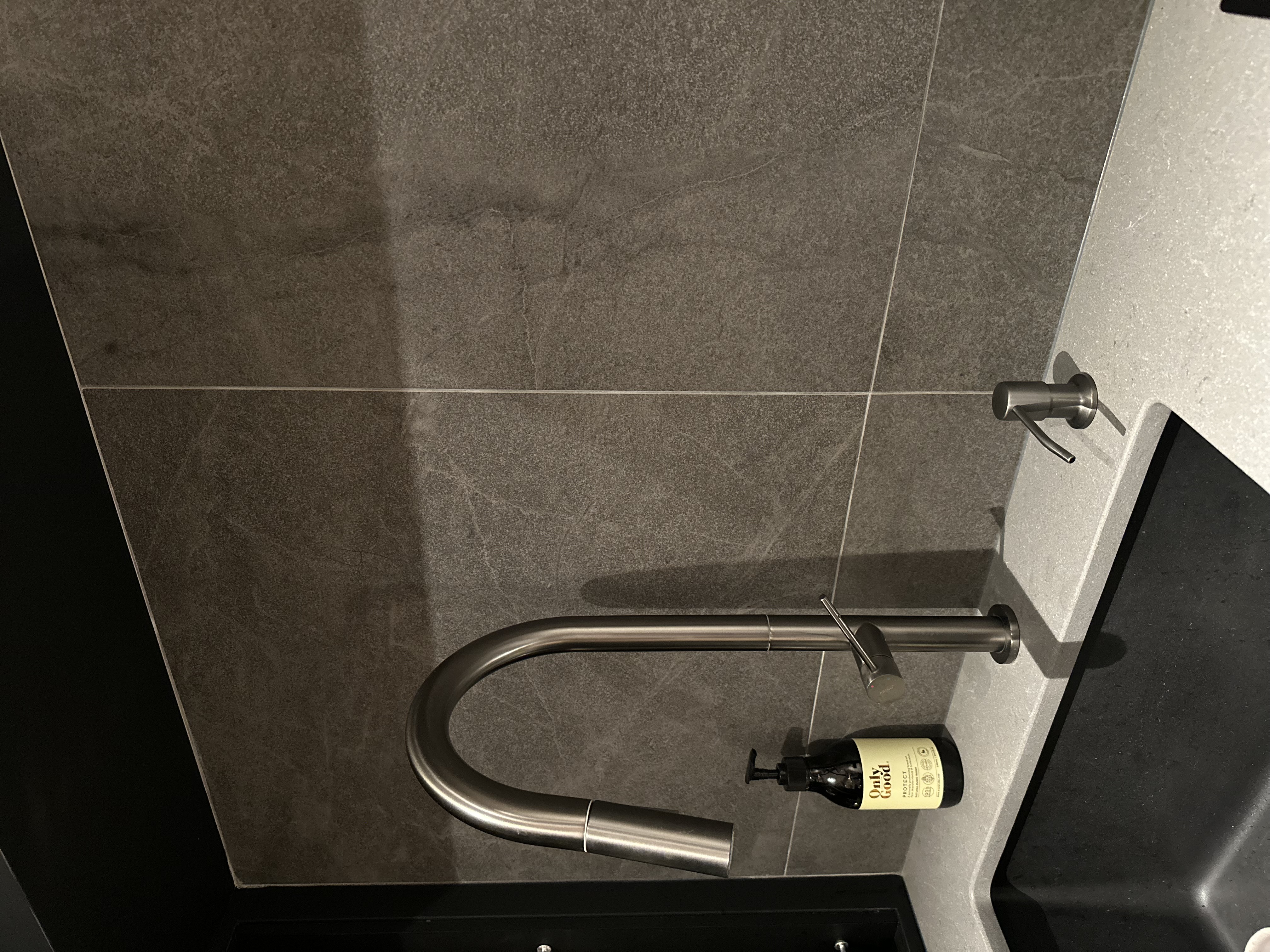 A modern dark themed kitchen  - Grey marble tiles, sleek faucet, modern bathroom, stainless steel handle, black countertop