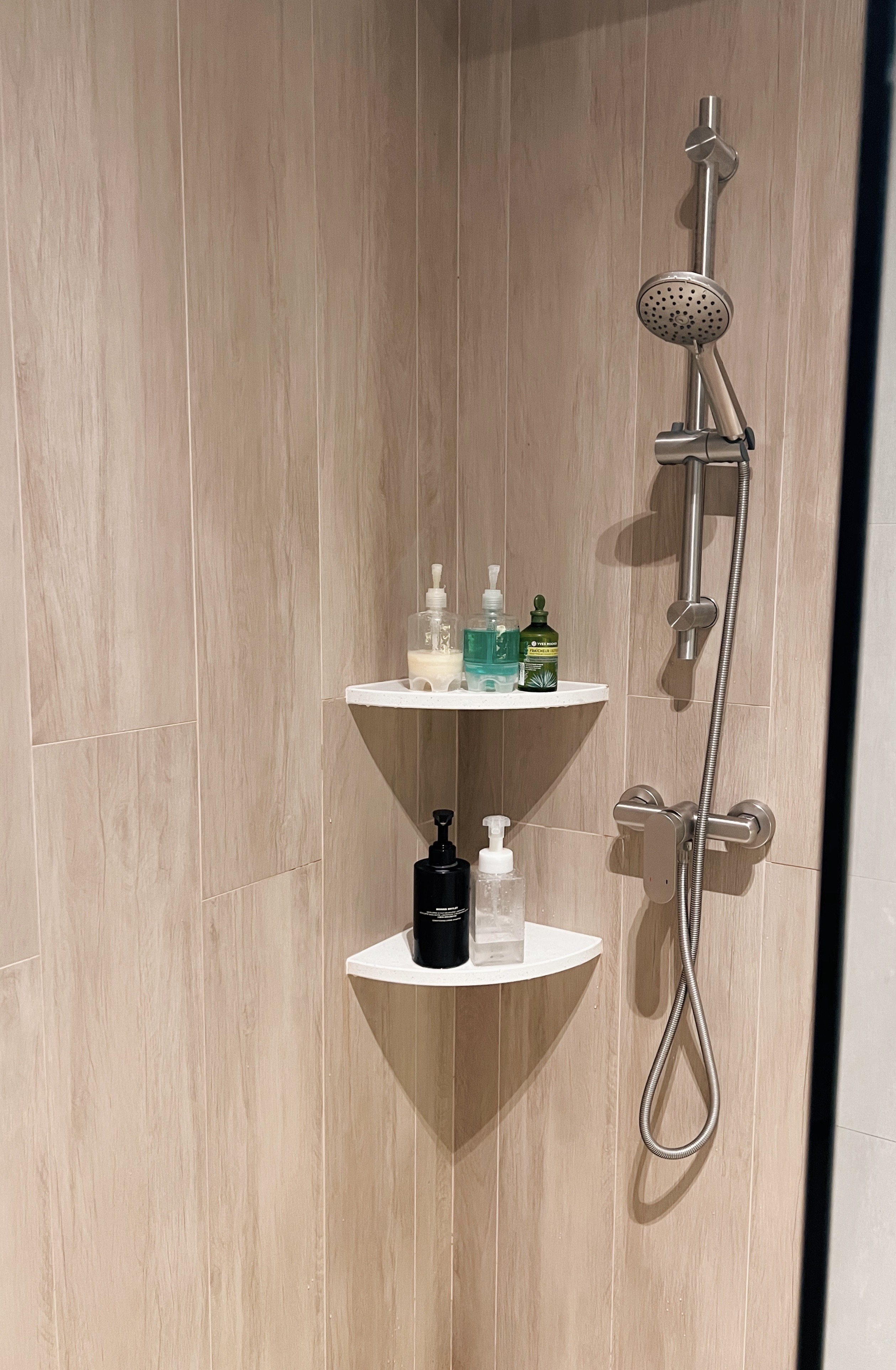 Entering a state of relaxation in our bathrooms - Shower area with integrated shelves, light wooden paneling, modern