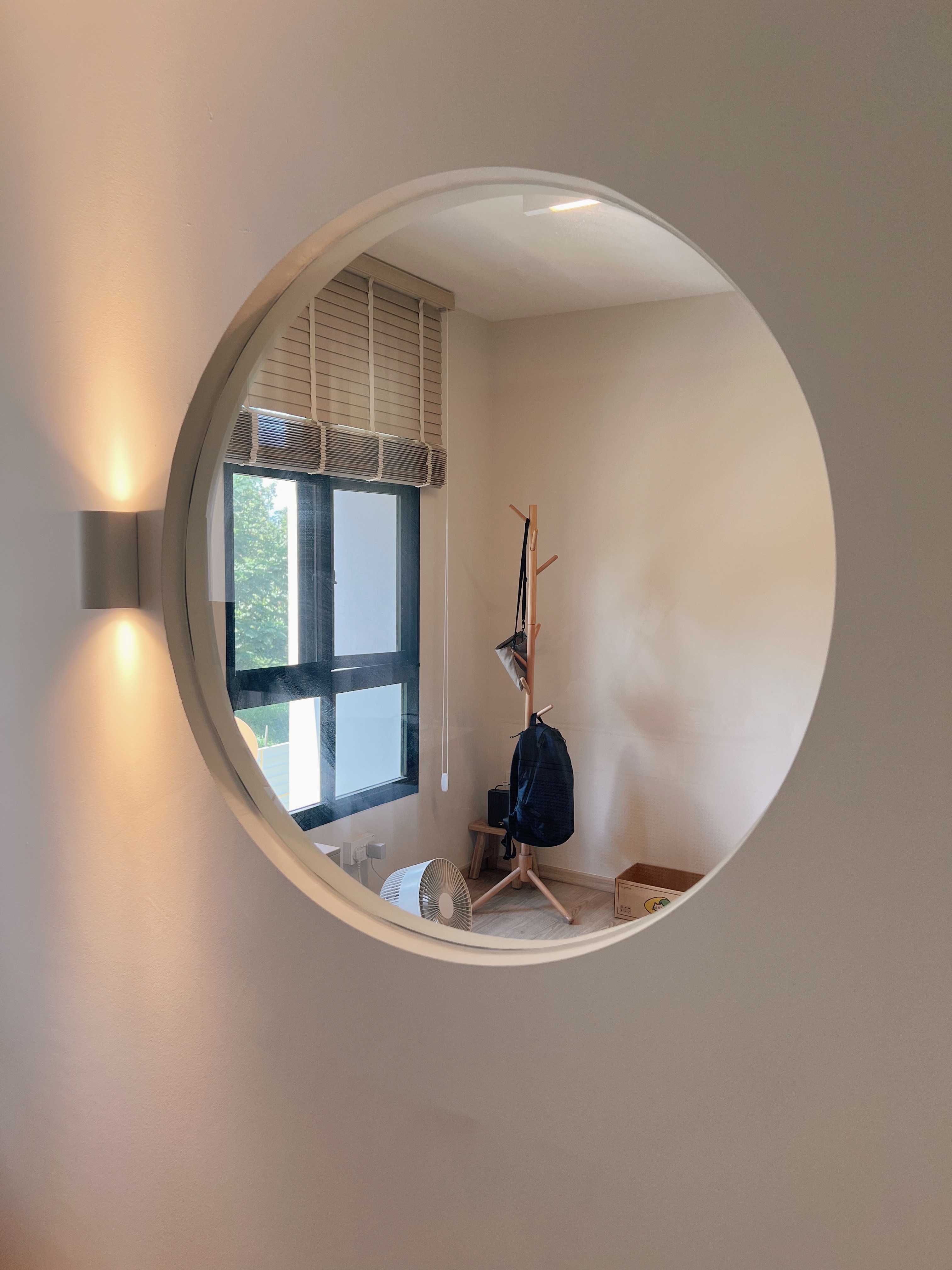 Finding focus in our home office - Circular window, light fixture, beige walls, wooden stand, black backpack, white fan
