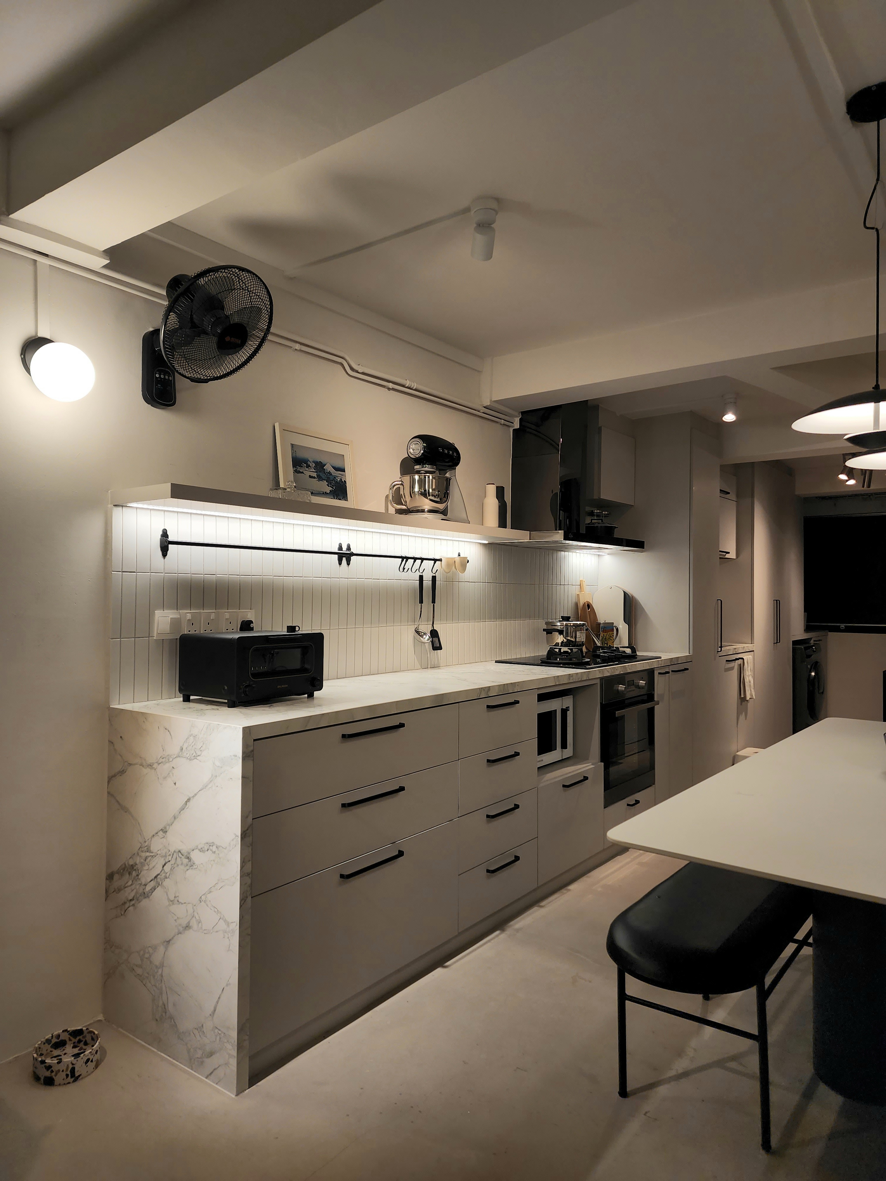 Transforming a 1980s wall kitchen - Modern kitchen with sleek design, white marble countertops, black appliances, pendant