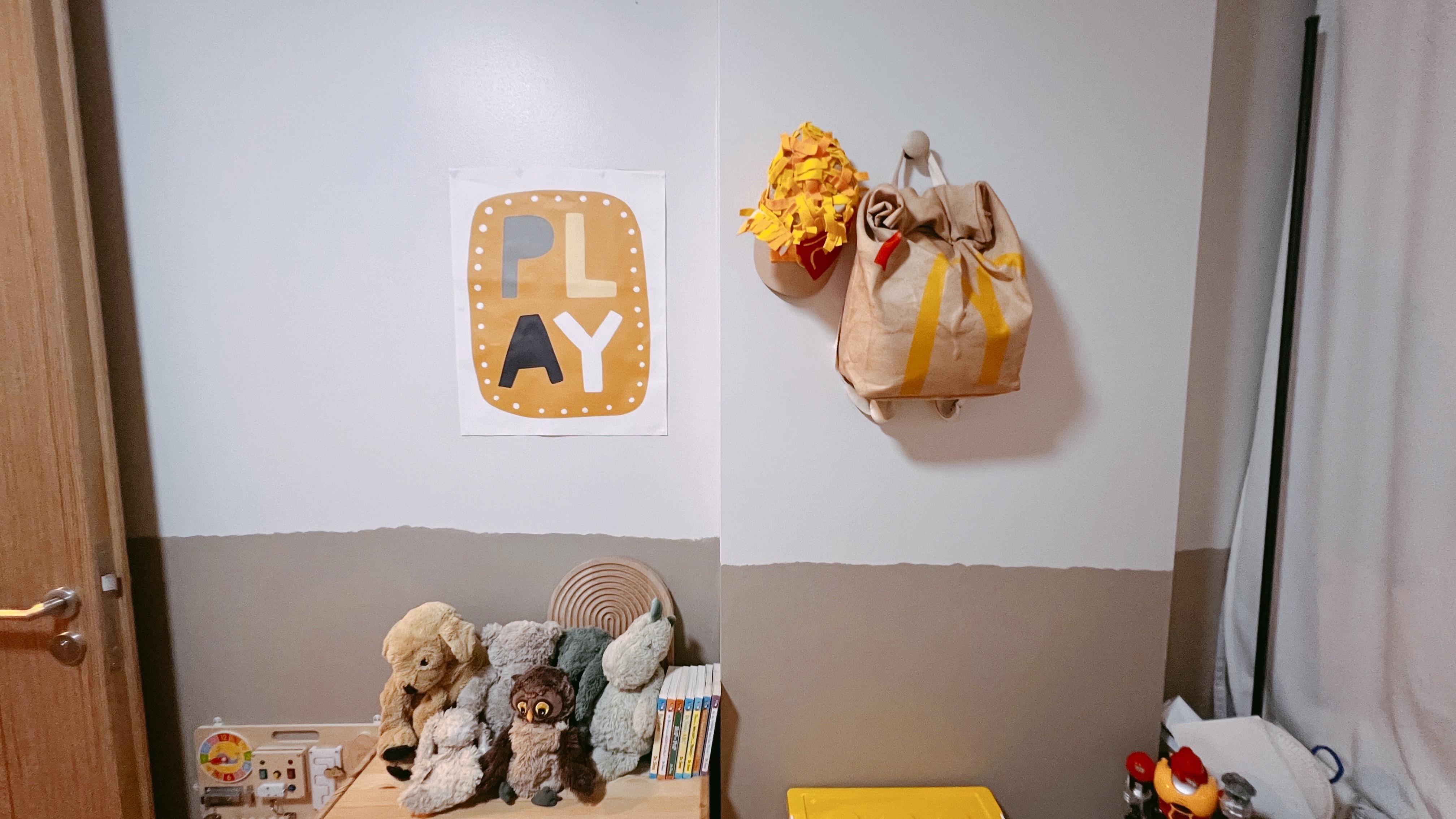 Welcome To Our Two Year Old’s Crib! - Wall art, plush toys, wooden shelf, colorful books, beige wall, wooden door, yellow