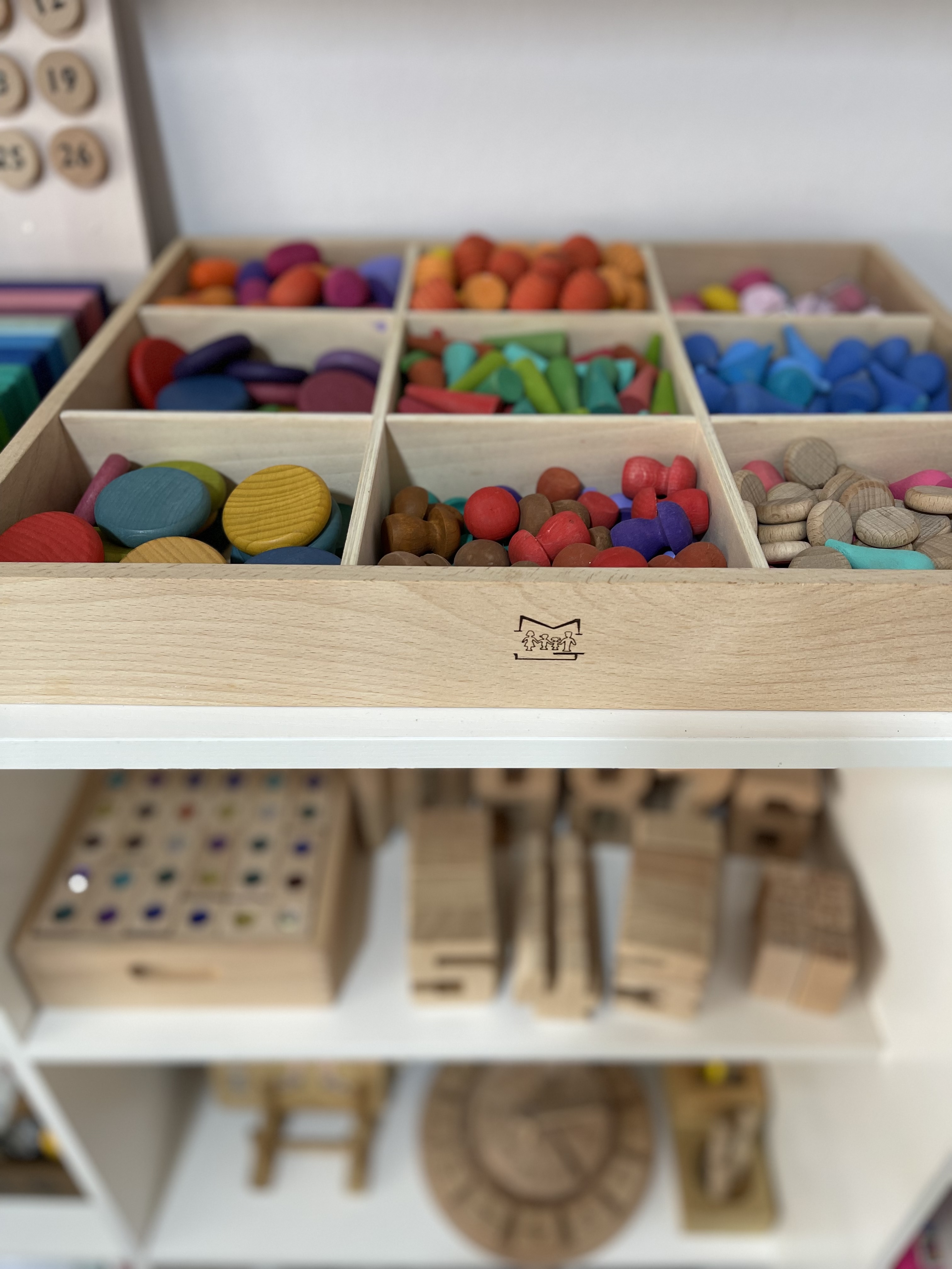 Montessori-inspired play corner - Wooden toy storage bins filled with colorful wooden blocks, each bin containing a variety