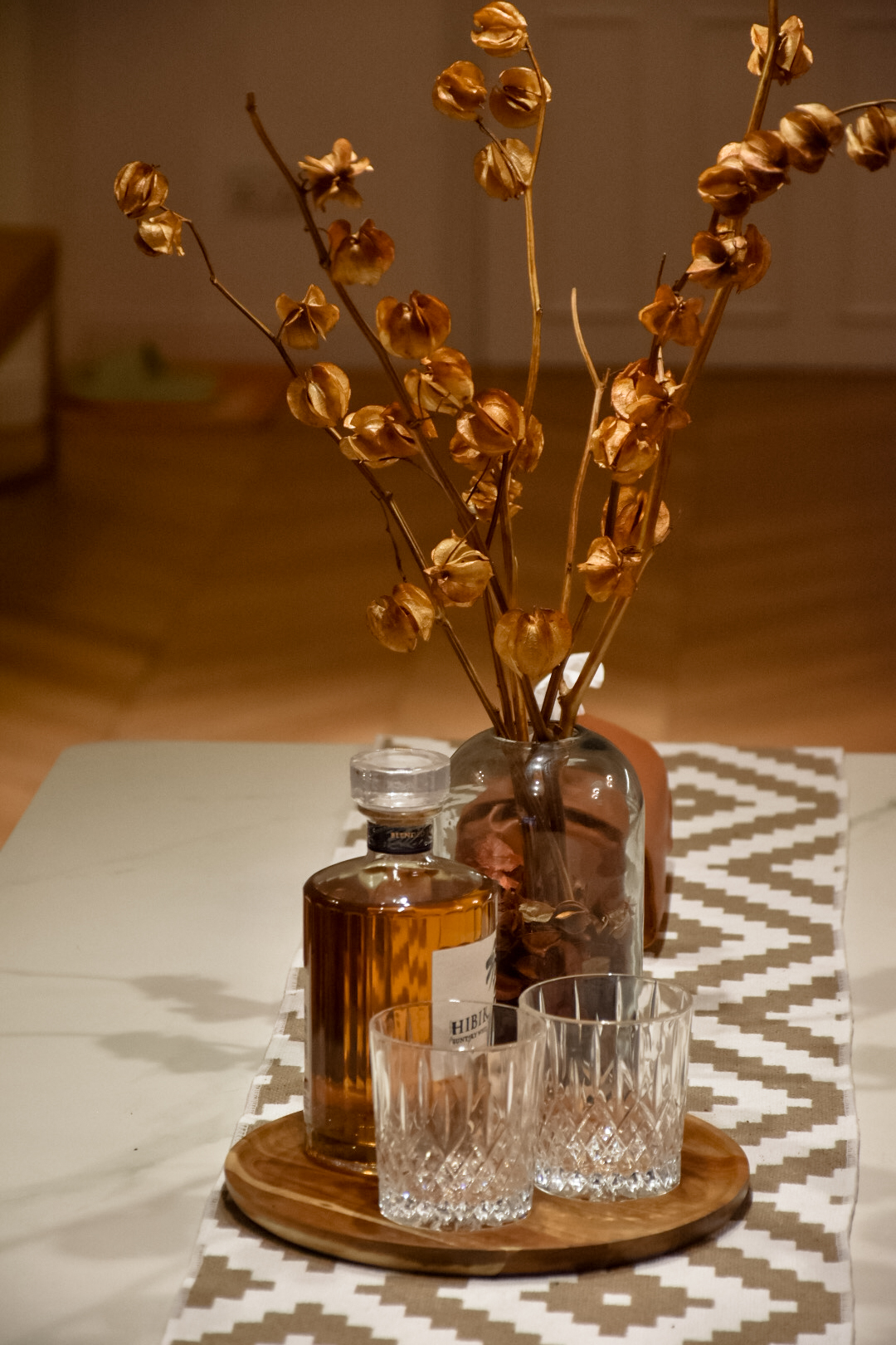 Gather - Dine  - Delight - vibrant amber liquor bottle, elegant glassware, rustic wooden tray, intricate crystal glasses