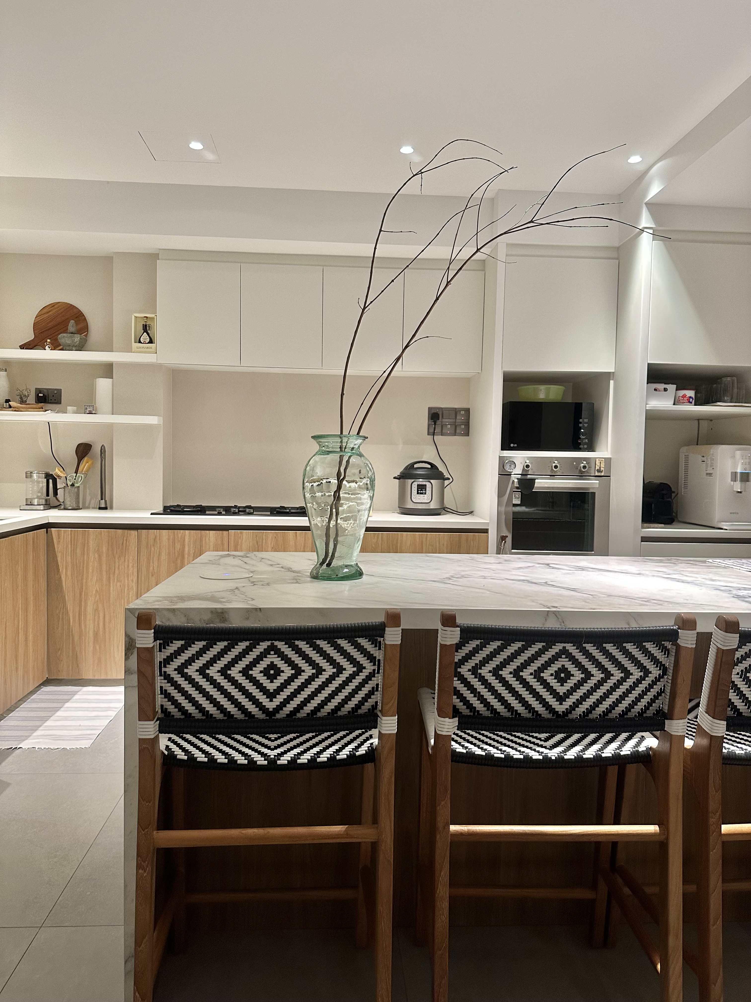 60’s grilles in a newly constructed house - Modern kitchen with marble island, wooden chairs with black and white patterned