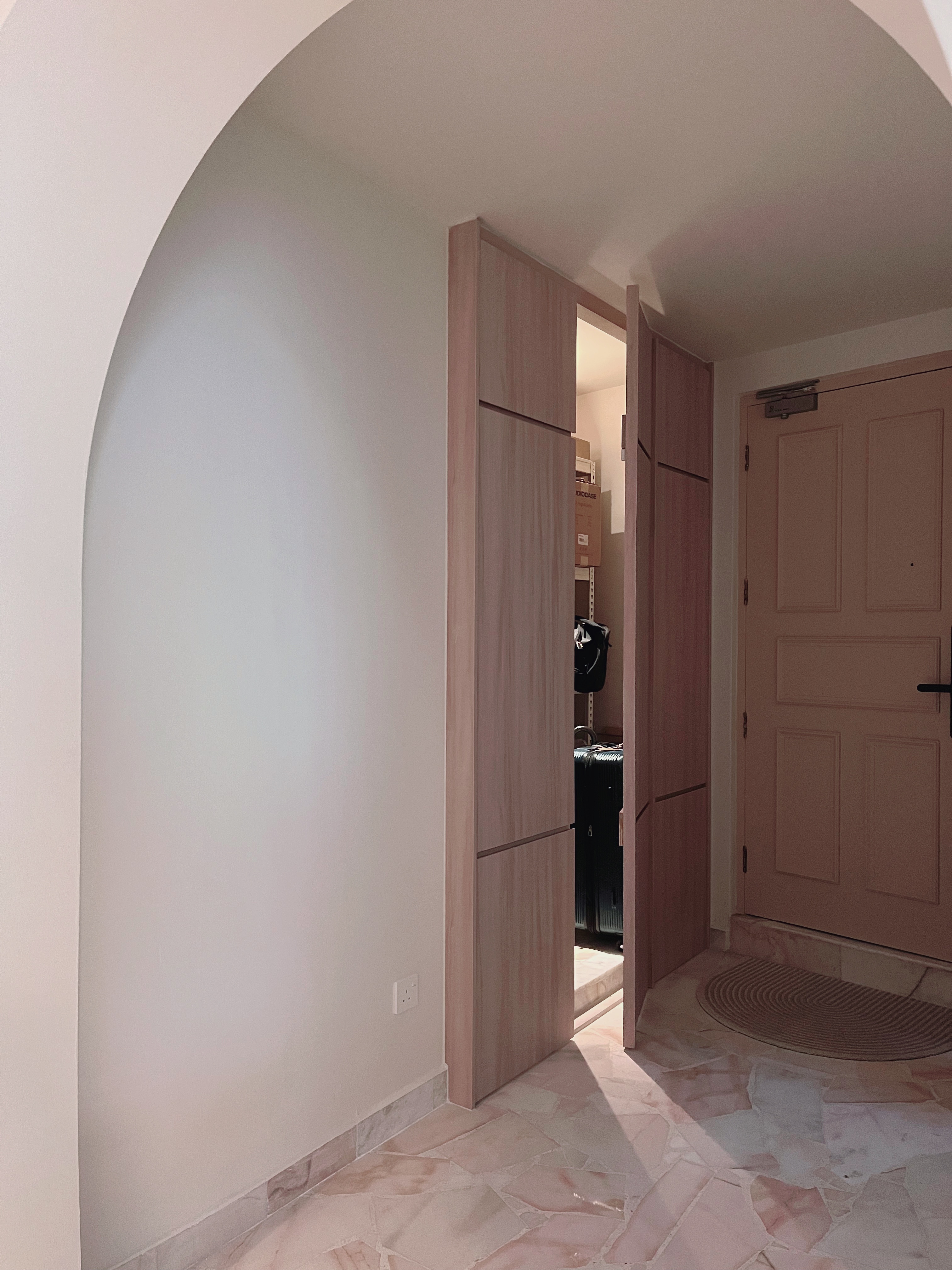 A warm and spacious foyer with a functional twist - Light-colored walls, archway, wooden doors, open doorway, light-colored