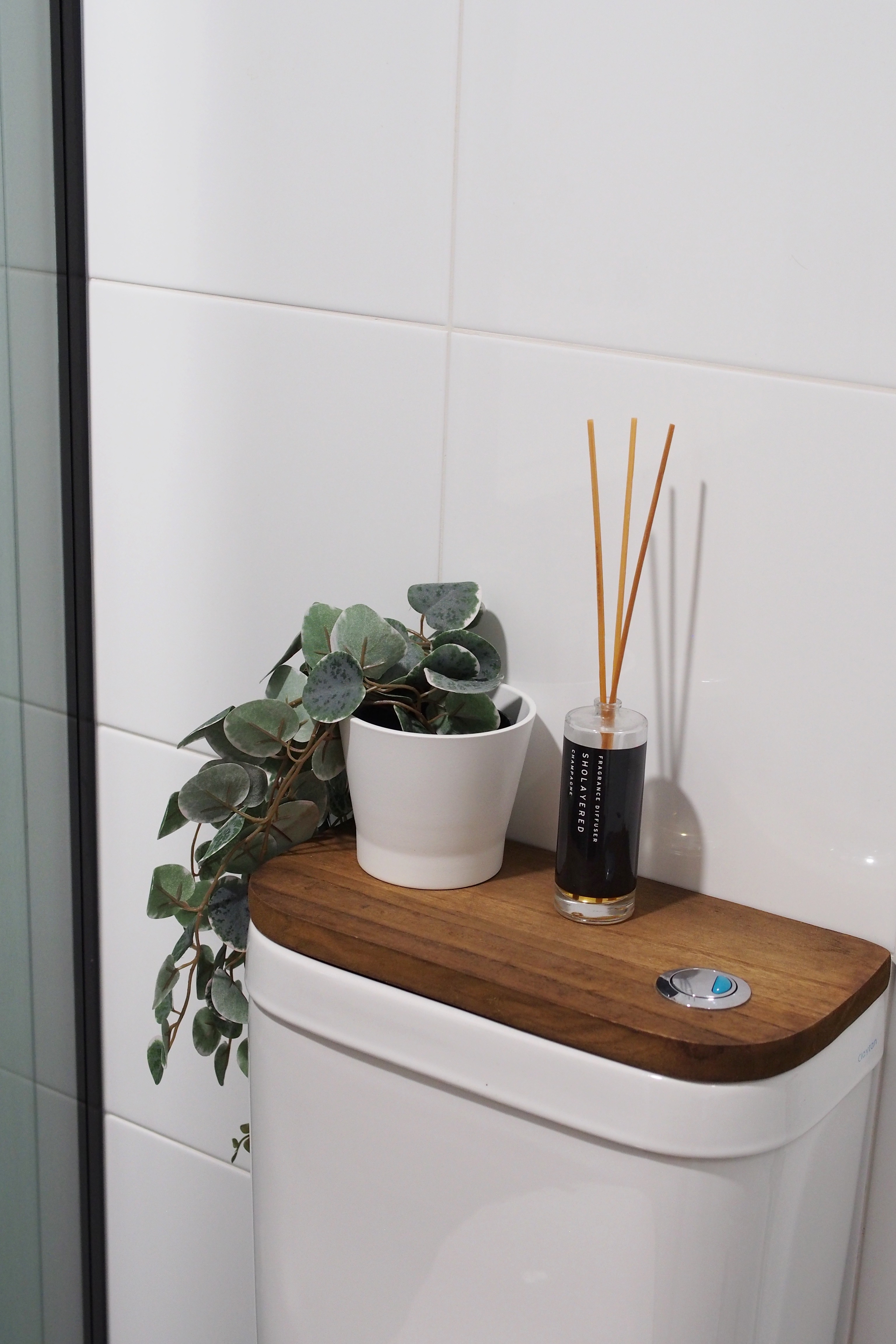 Making a bathroom with HDB fittings work - White tiled wall, wooden toilet tank, green potted plant, white ceramic pot