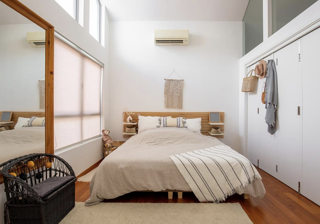 Californian Boho Style Attic Living - Sunlit bedroom with large windows, wooden floor, beige bedding, striped blanket, wicker