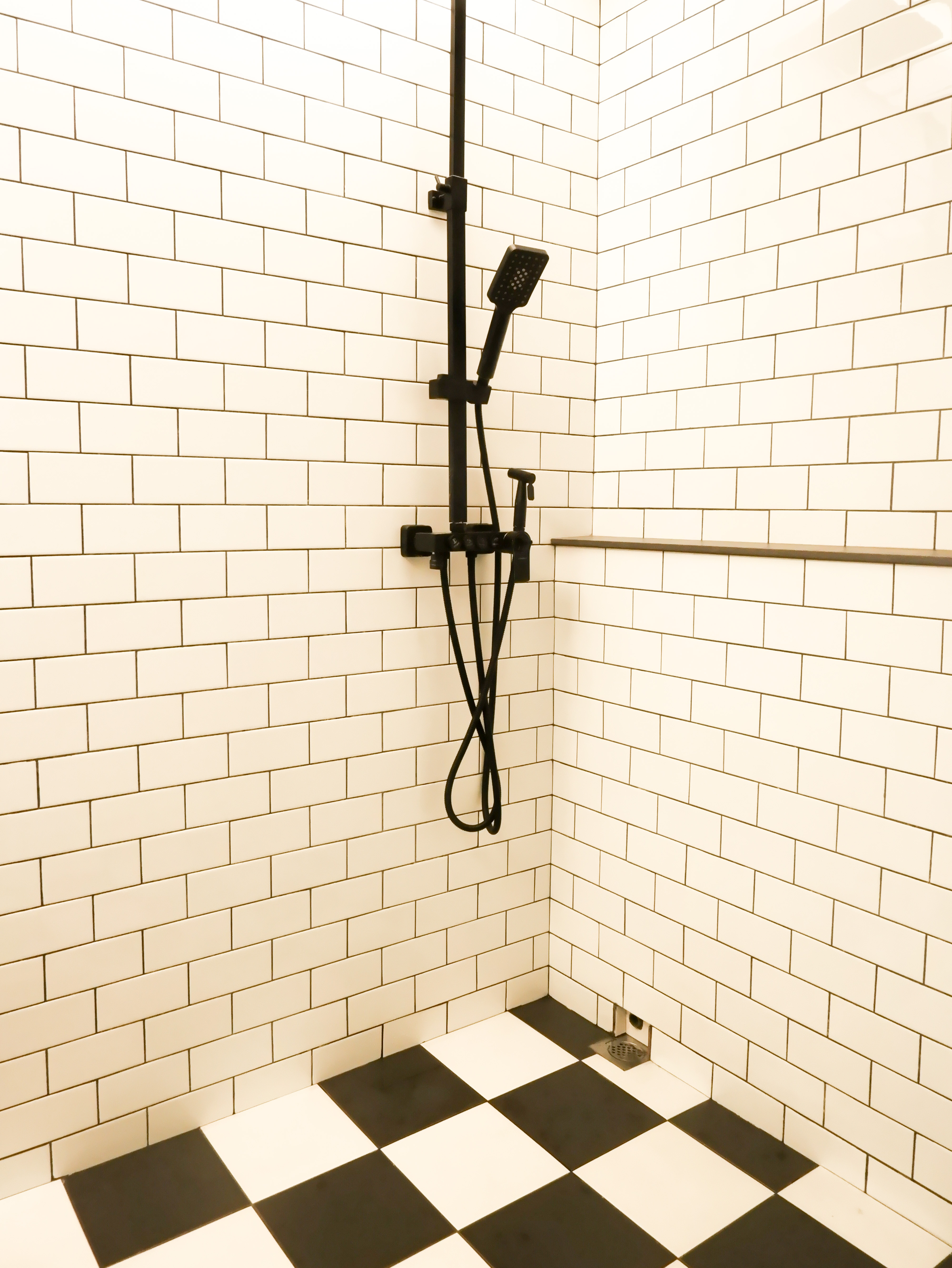 Build Your Own Toilet  - White tiled wall, black showerhead, black hose, black shower fixture, black and white checkered