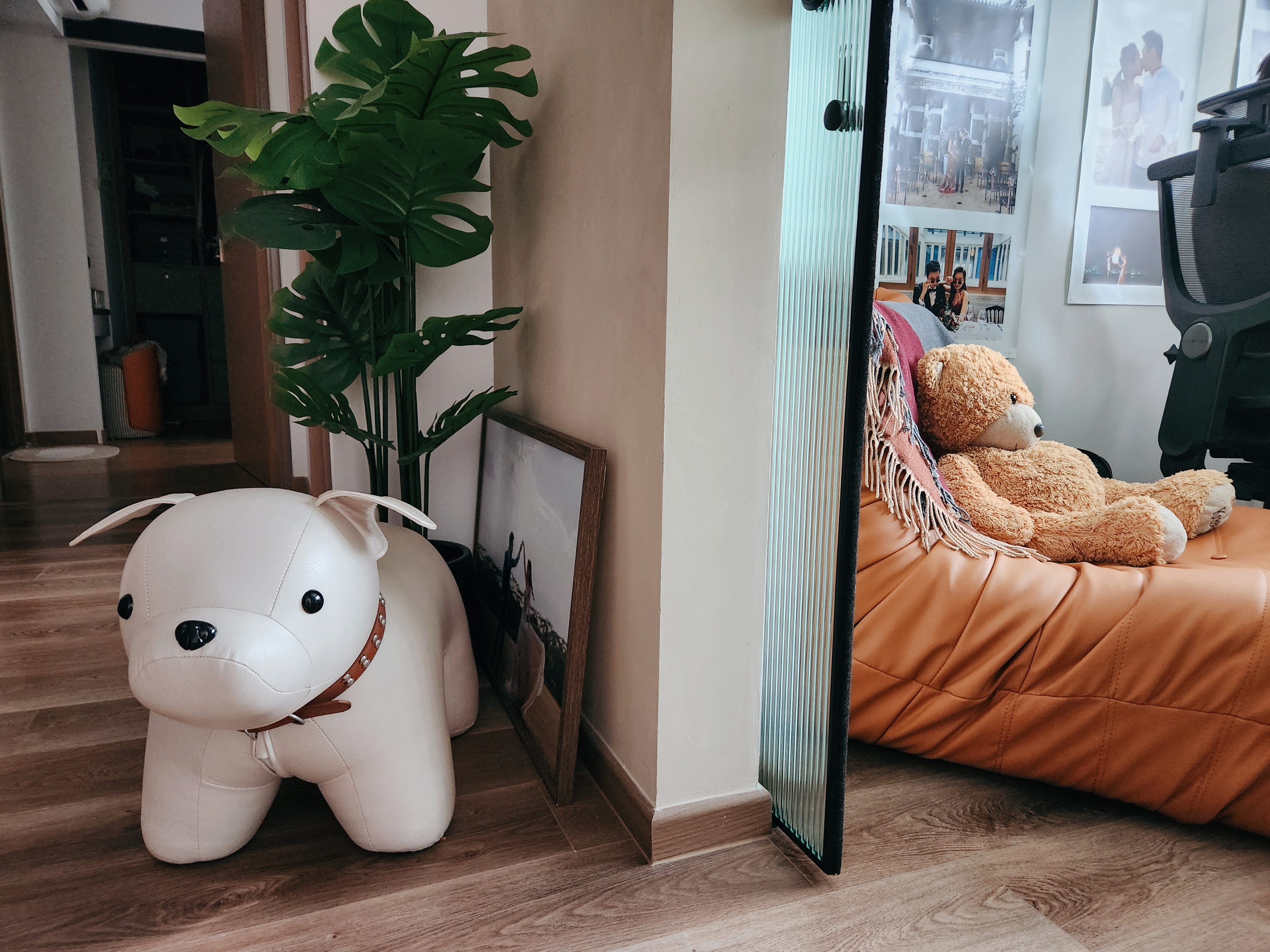 Take a peek behind our curved wall 👀 - White plush dog, orange leather couch, brown teddy bear, green potted plant, framed