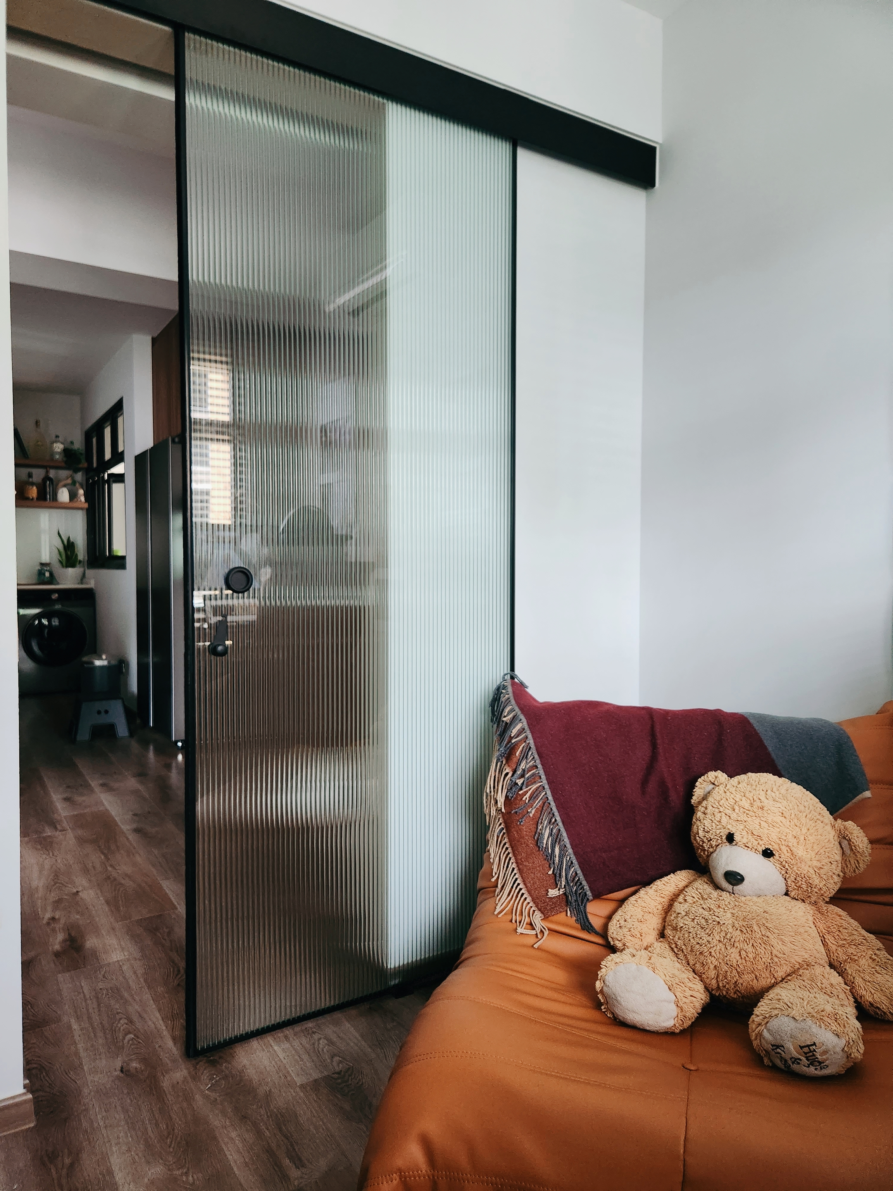 Take a peek behind our curved wall 👀 - Glass door, modern interior, wooden floor, orange sofa, teddy bear, colorful pillows
