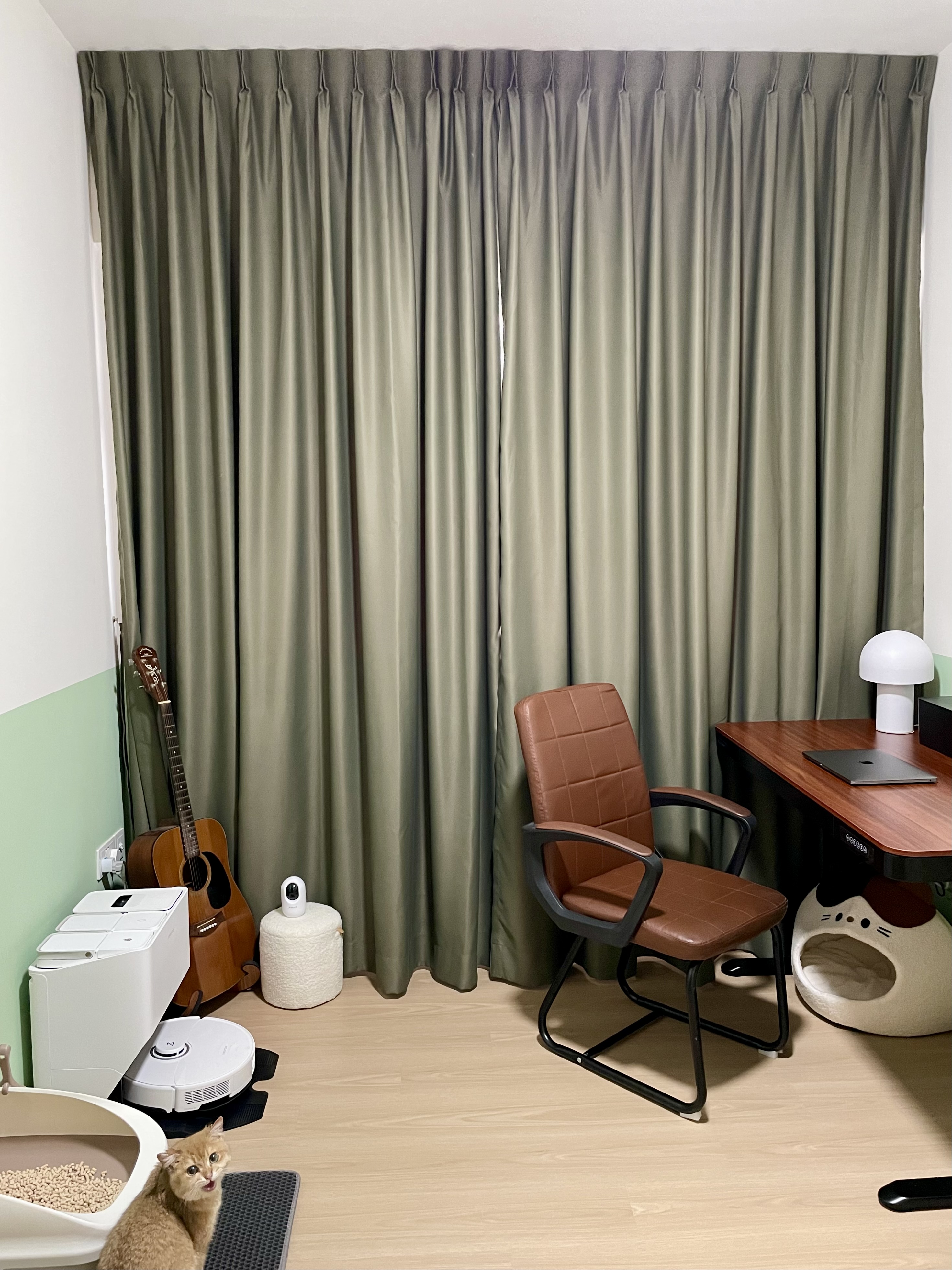 Multipurpose Room - Study + Cat Room - Green curtains, wooden desk, brown leather chair, white robotic vacuum, beige cat