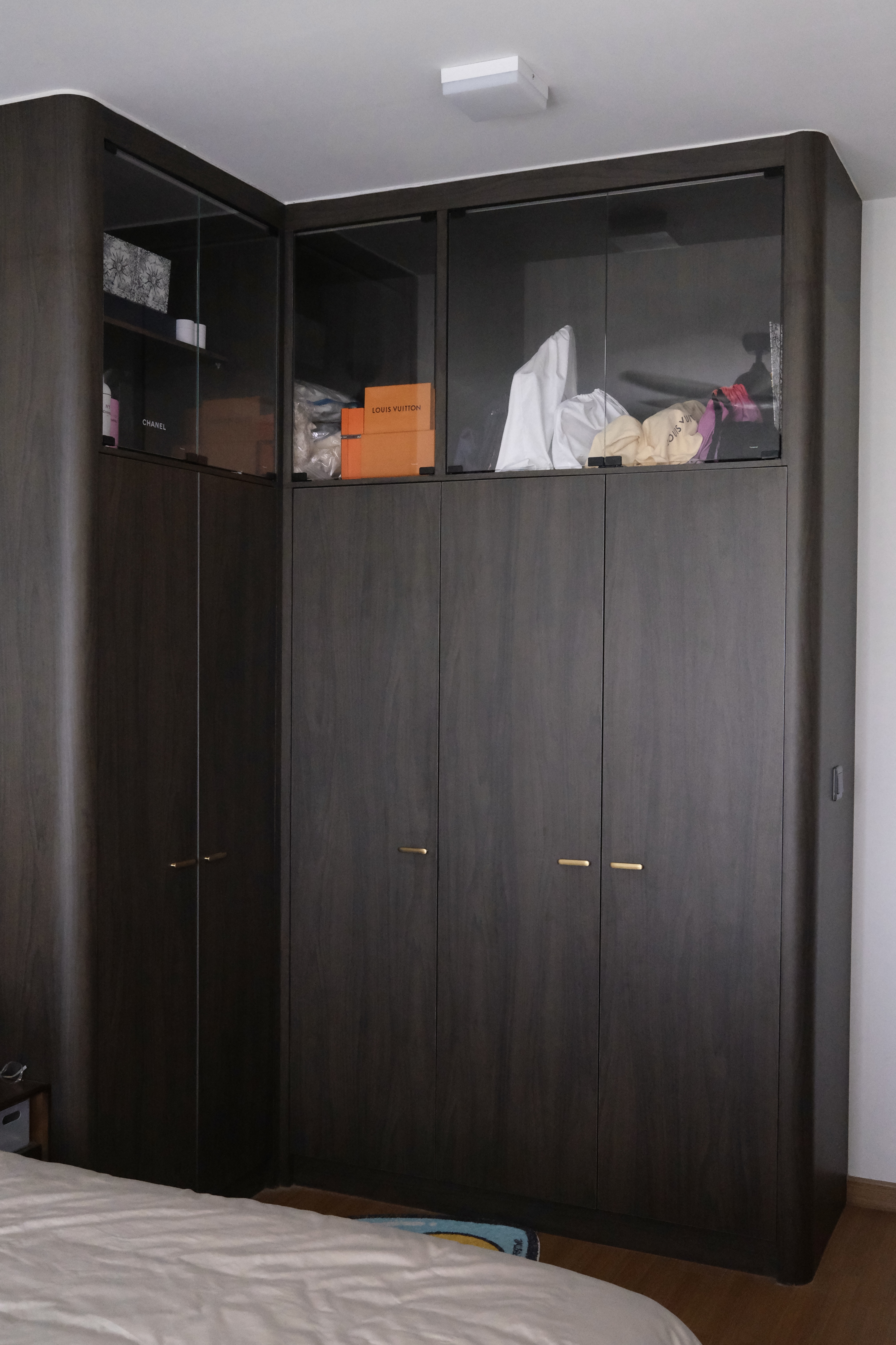The Primary | Where we recharge - Dark wooden wardrobe with glass doors, neatly organized closet, white bed with beige