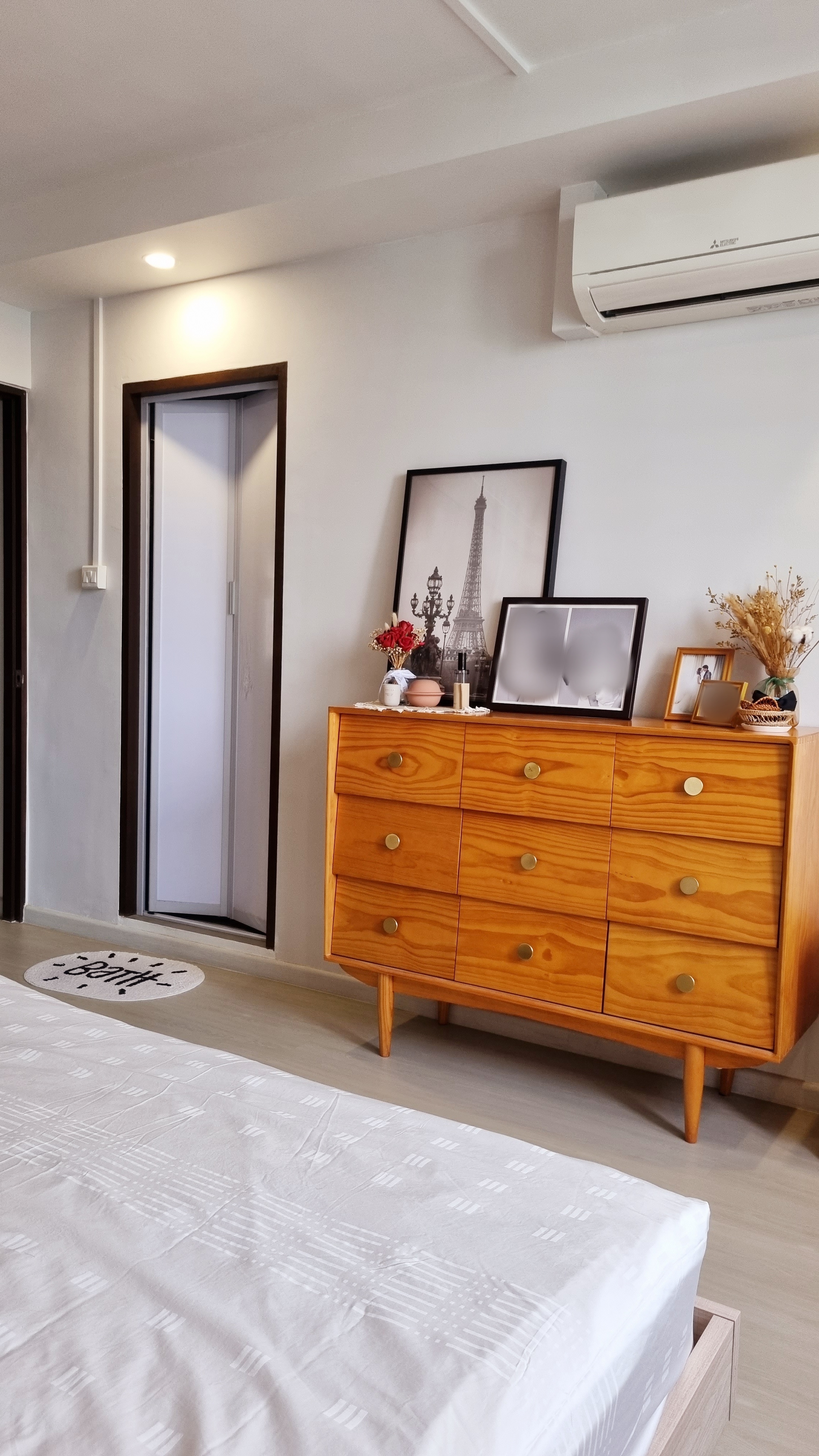 Our mix and match MASTERBEDROOM - Wooden dresser with brass handles, white bedspread with subtle patterns, air conditioning