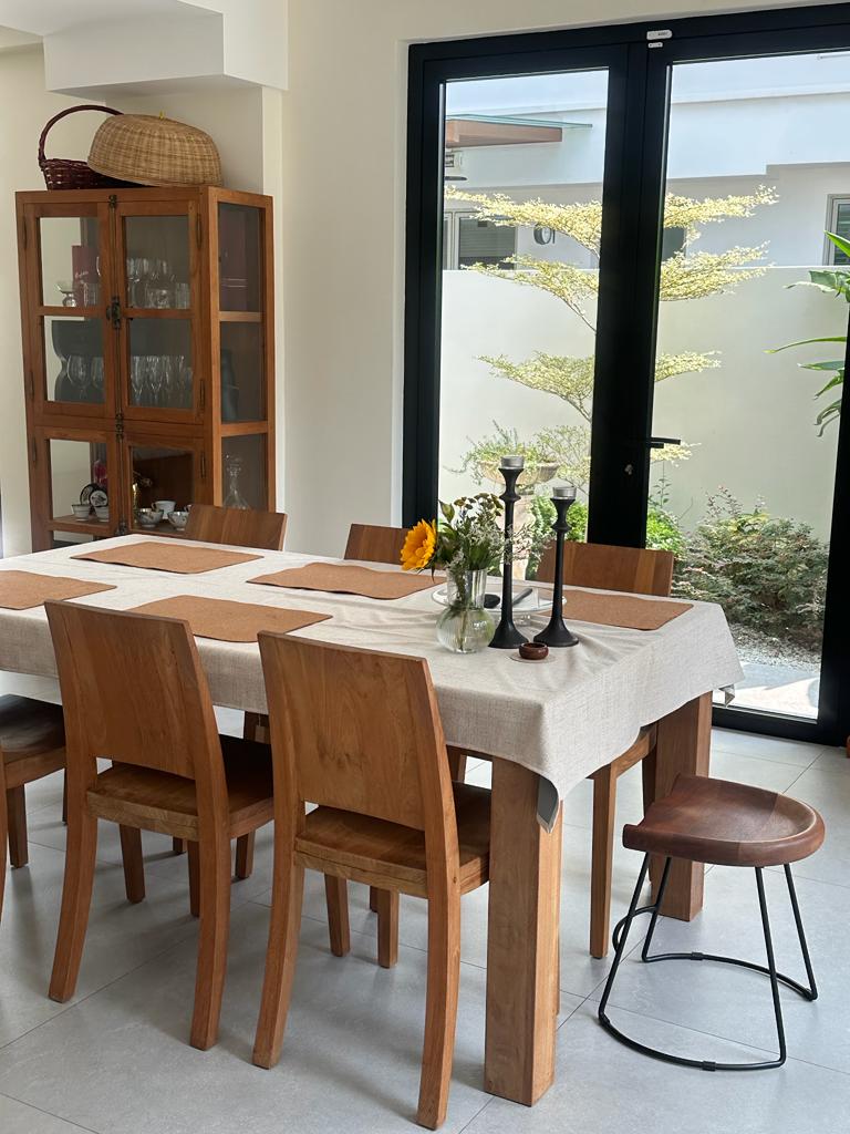 Indoor dining room with an outdoor feel - Wooden dining table, beige tablecloth, wooden chairs, black metal stool, large