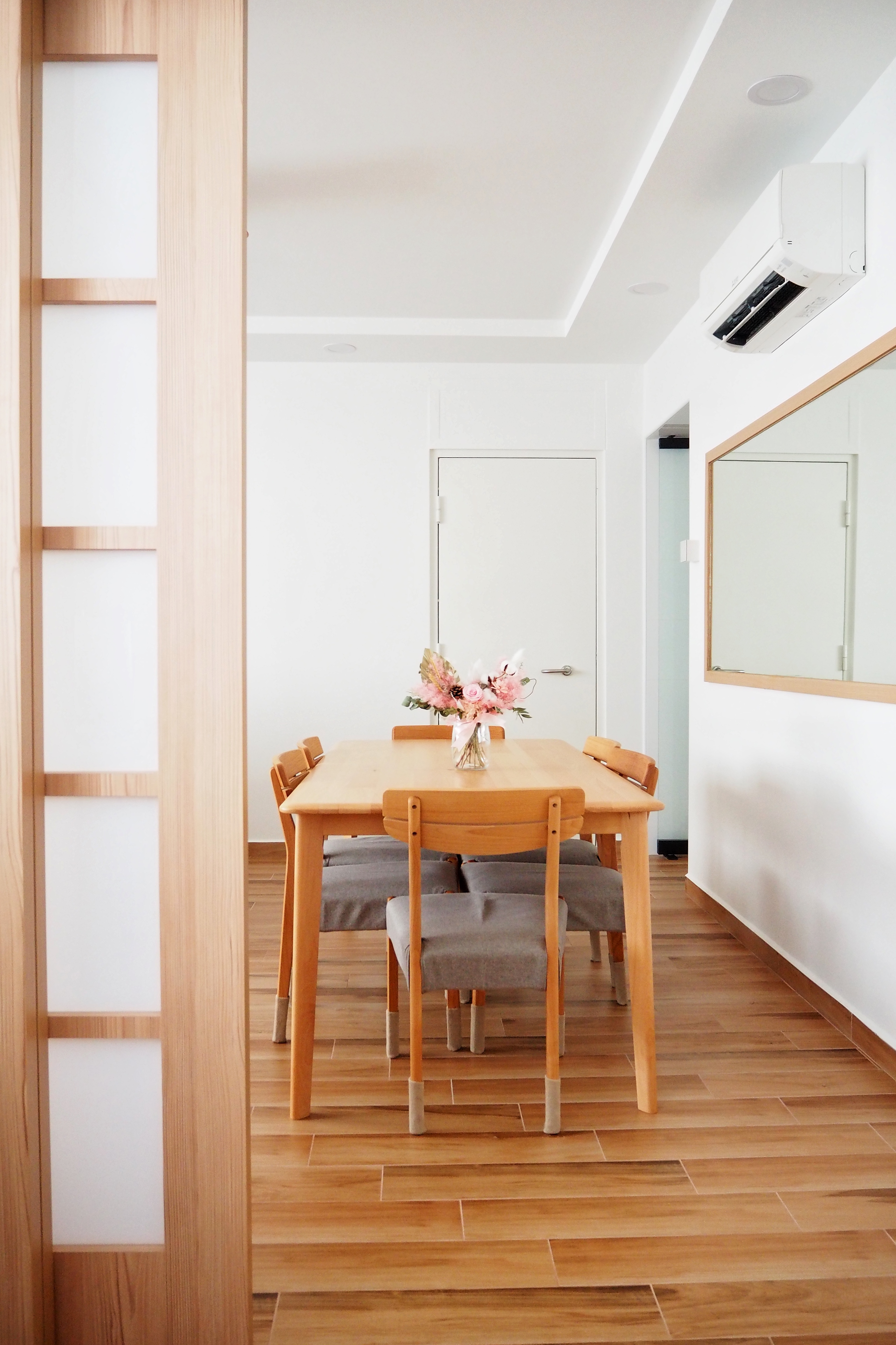 Our Serene Dining Space - Wooden dining table, minimalist design, light wooden chairs, gray cushioned seats, vase with pink