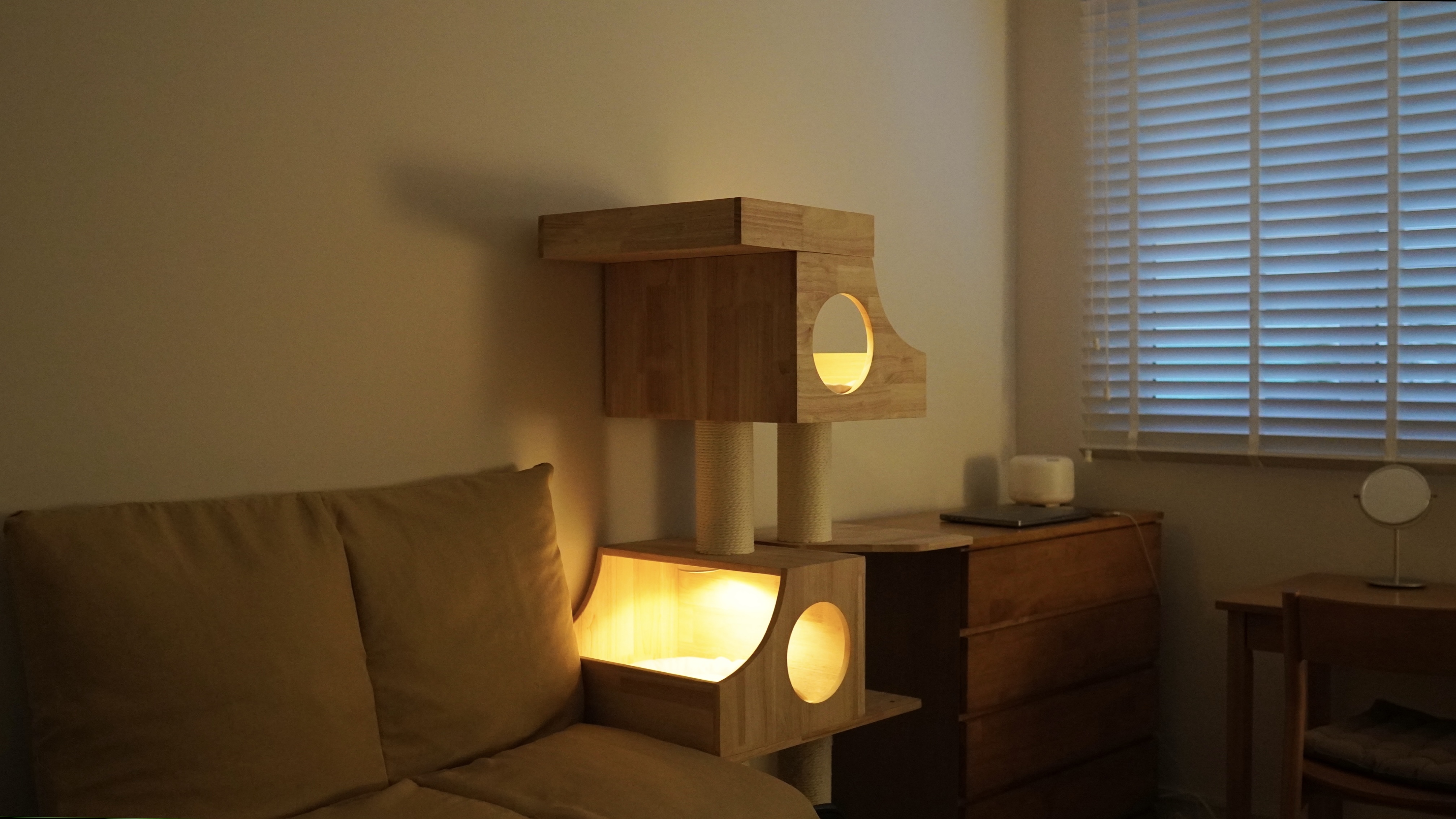 A Comforting Night Routine for New Homeowners - Wooden cat tree with illuminated circular openings, cozy beige couch, soft