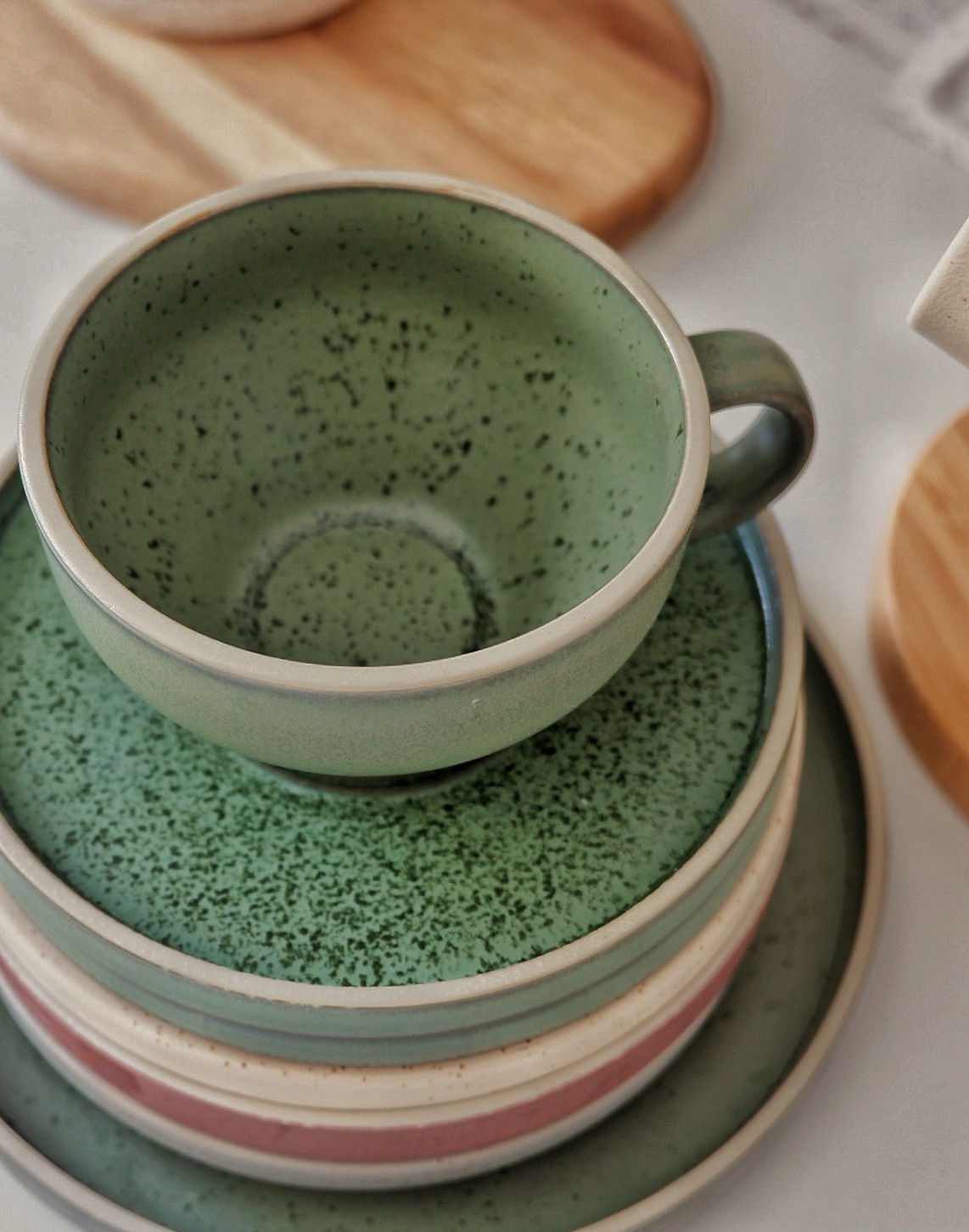 Our Home collections - Green ceramic mug, stacked plates, speckled design, rustic aesthetic, earthy tones, natural texture