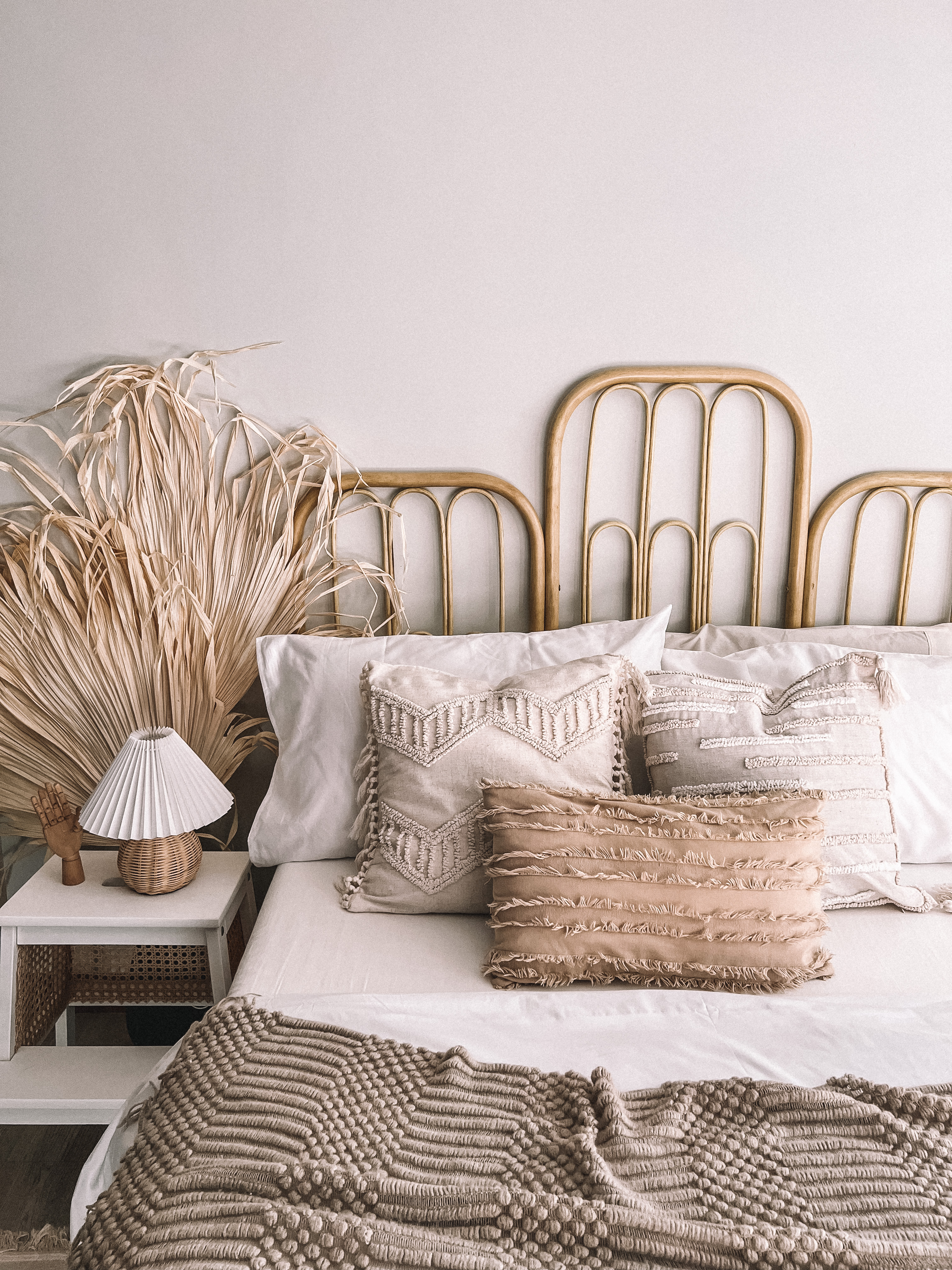 Tips on getting a boho bedroom - Wooden bed frame, beige and white pillows, textured throw blanket, rustic lamp, natural