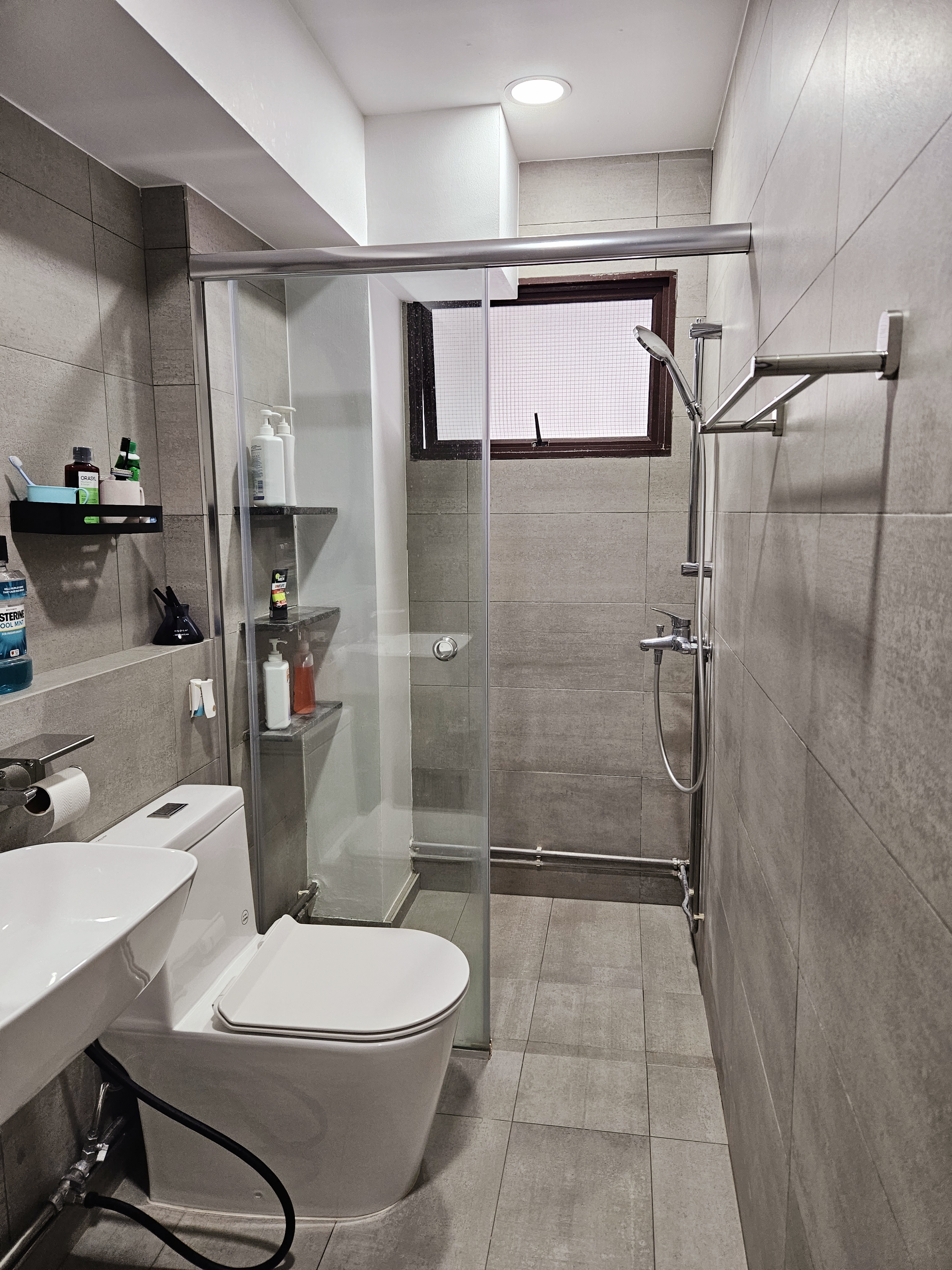 Our EARTHY Bathrooms - Modern bathroom with sleek design, gray tiles, white toilet, glass shower enclosure, built-in shelf