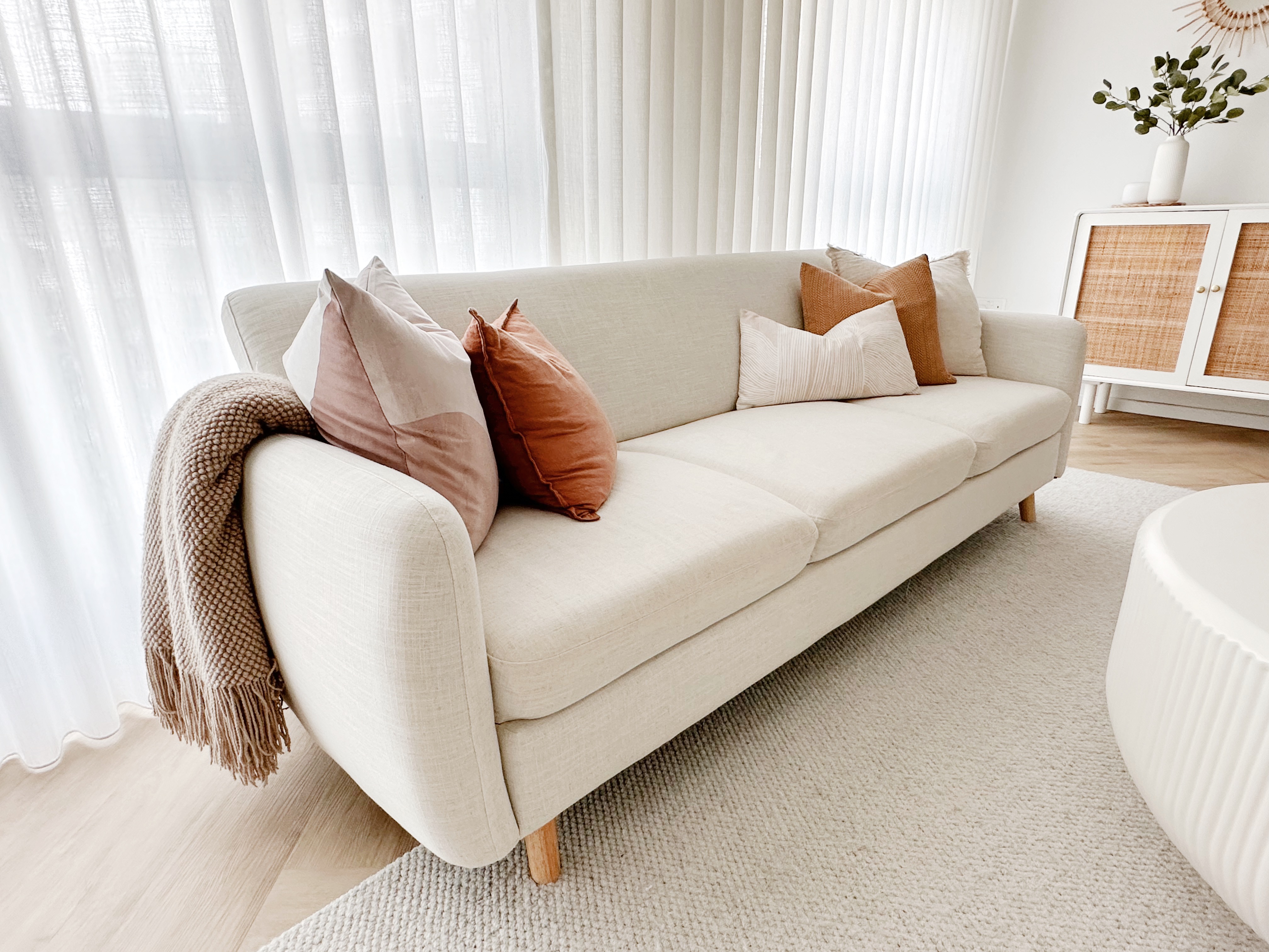 Our Cosy Corner - Cream-colored sofa, beige cushions, brown and beige pillows, sheer white curtains, light wooden floor