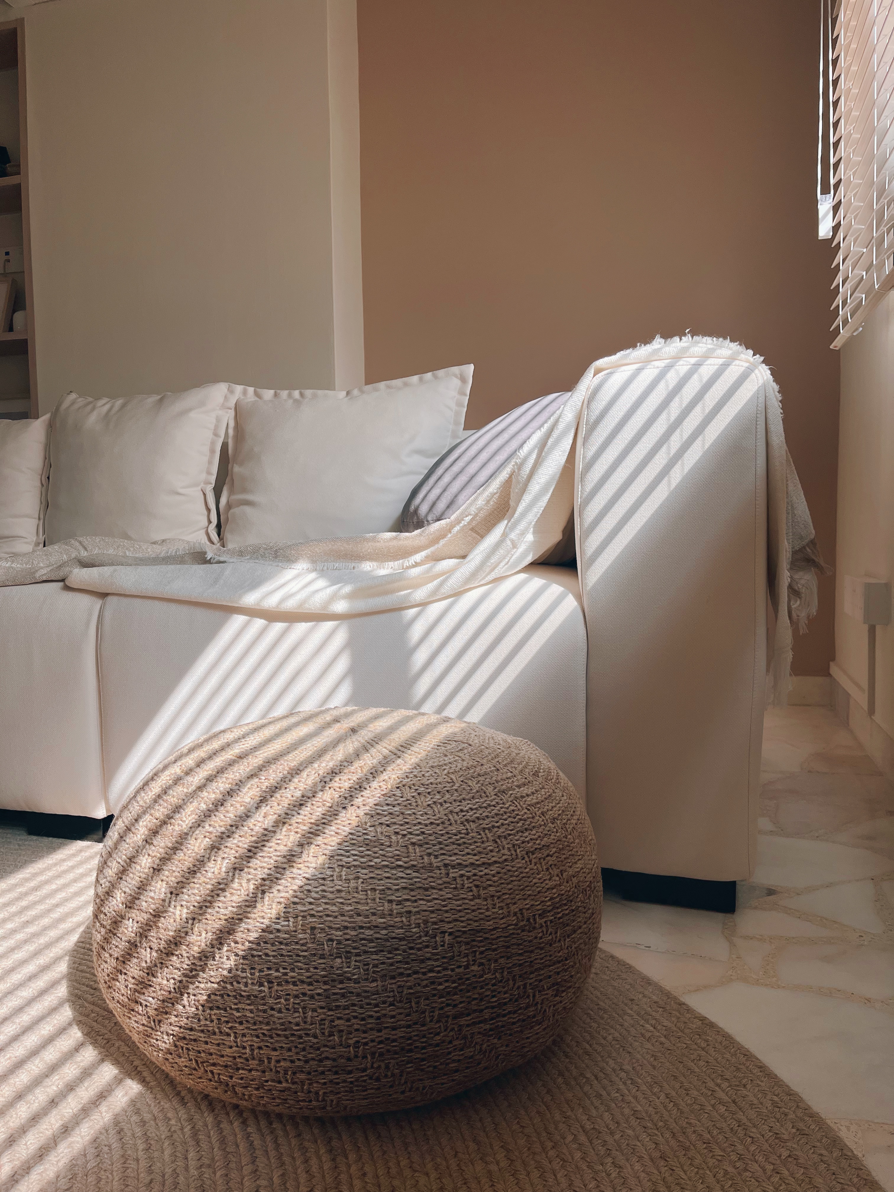 Cosiest nook for me-time and a book! - Sunlight streaming through blinds, soft beige sofa, white pillows, textured throw