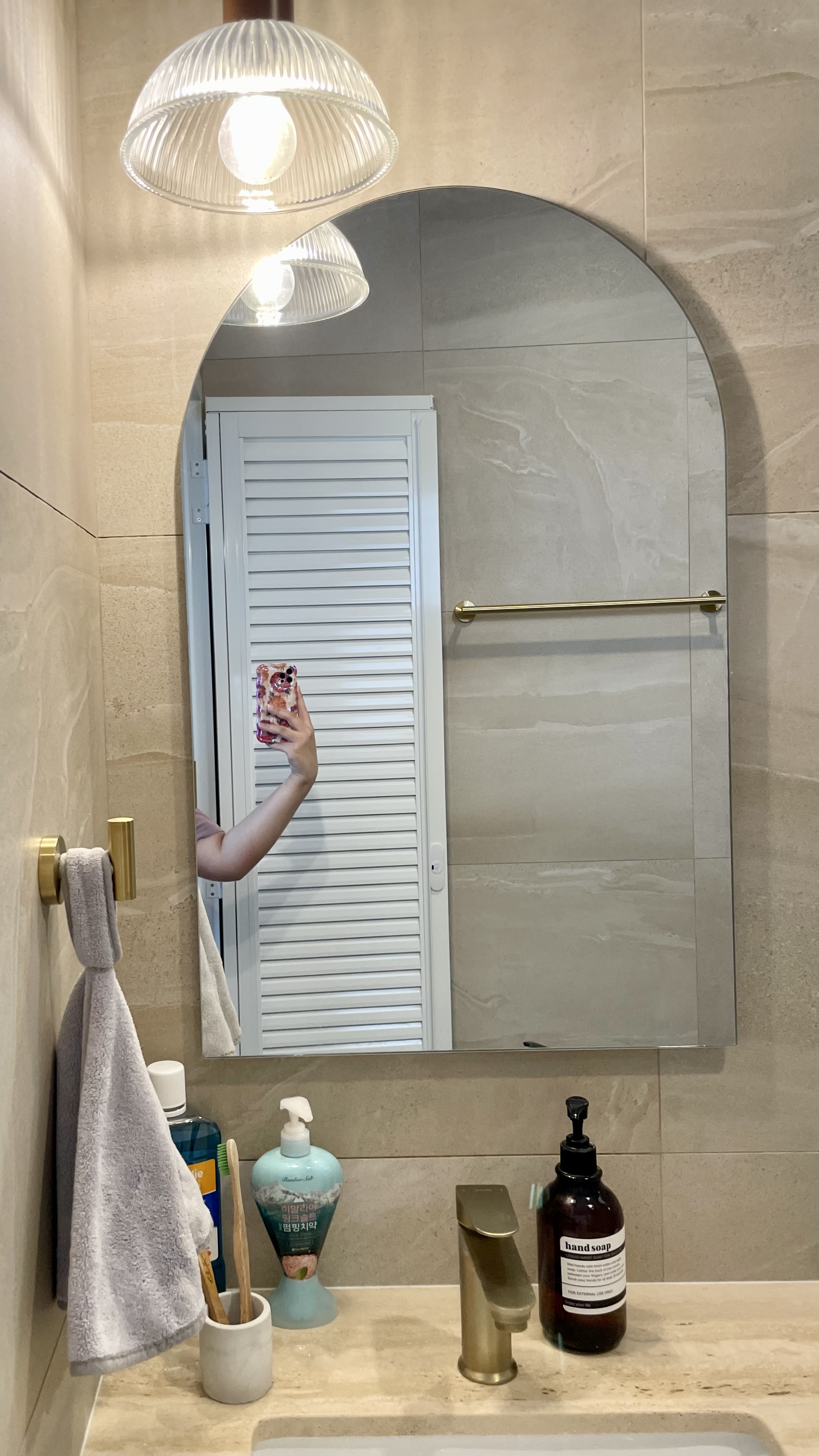 Travertine Hotel Bathroom in BTO - Bathroom mirror, white door, gold towel, gray towel, bathroom sink, soap dispenser, hand
