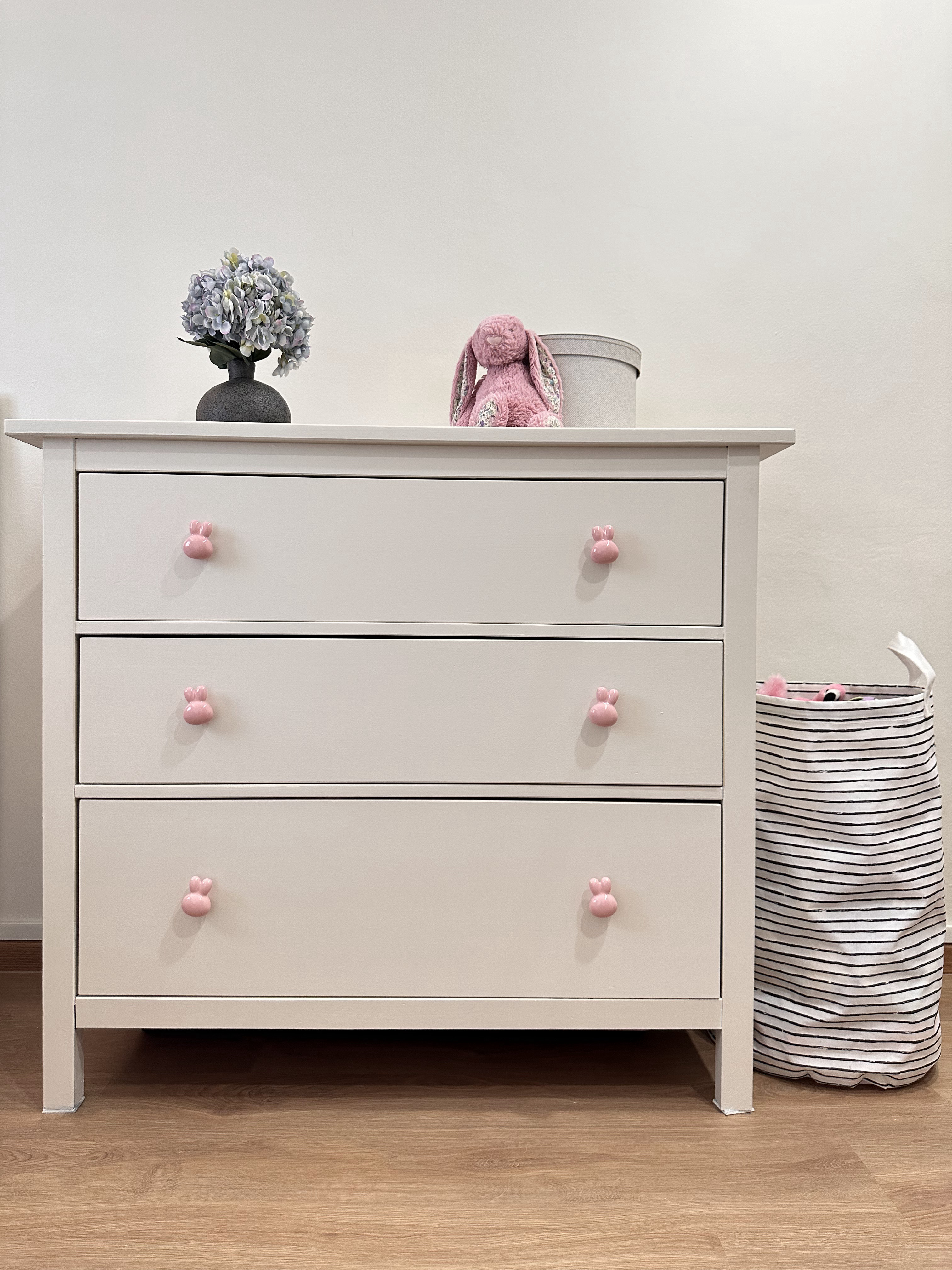 Designing our own modern farmhouse. - White dresser with pink bunny handles, lavender flowers in a vase, pink stuffed bunny