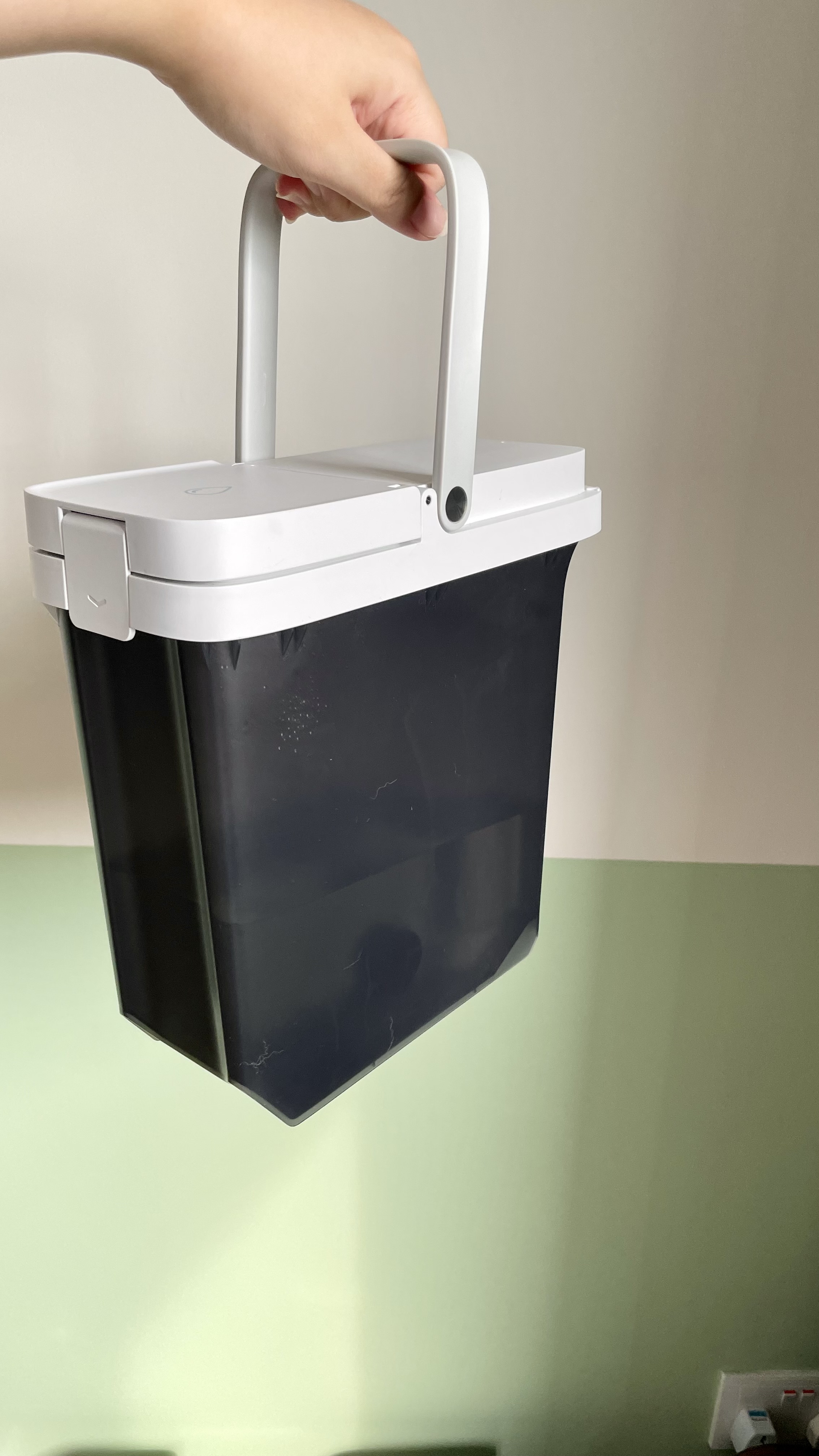 Must-have for busy homeowners - Robot Vacuum - White plastic trash bin, black trash bag, hand holding bin, minimalist design