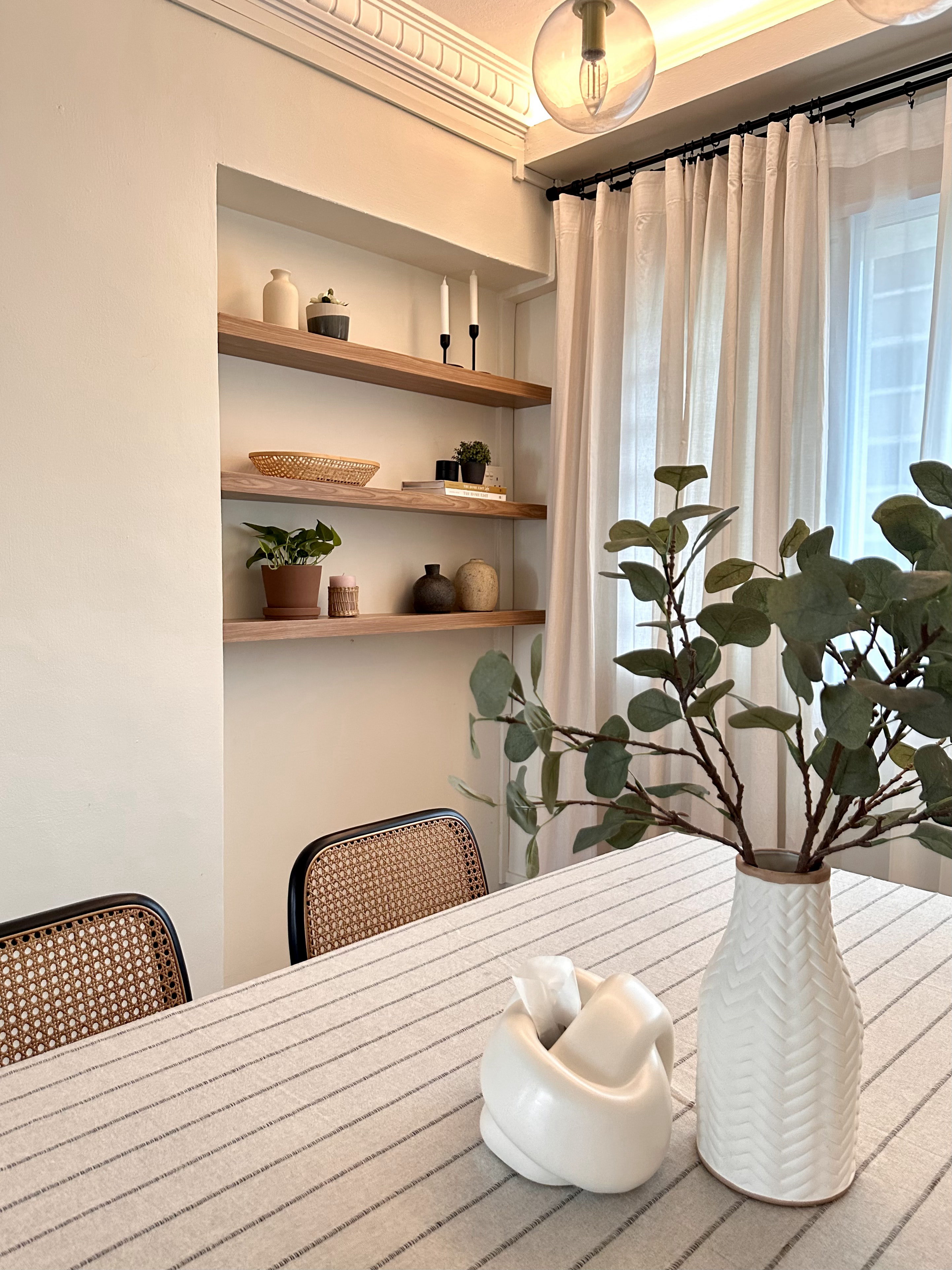 Mix and Match Dining Chairs - Light-colored walls, minimalist shelving, wooden shelves, white curtains, potted plant, woven