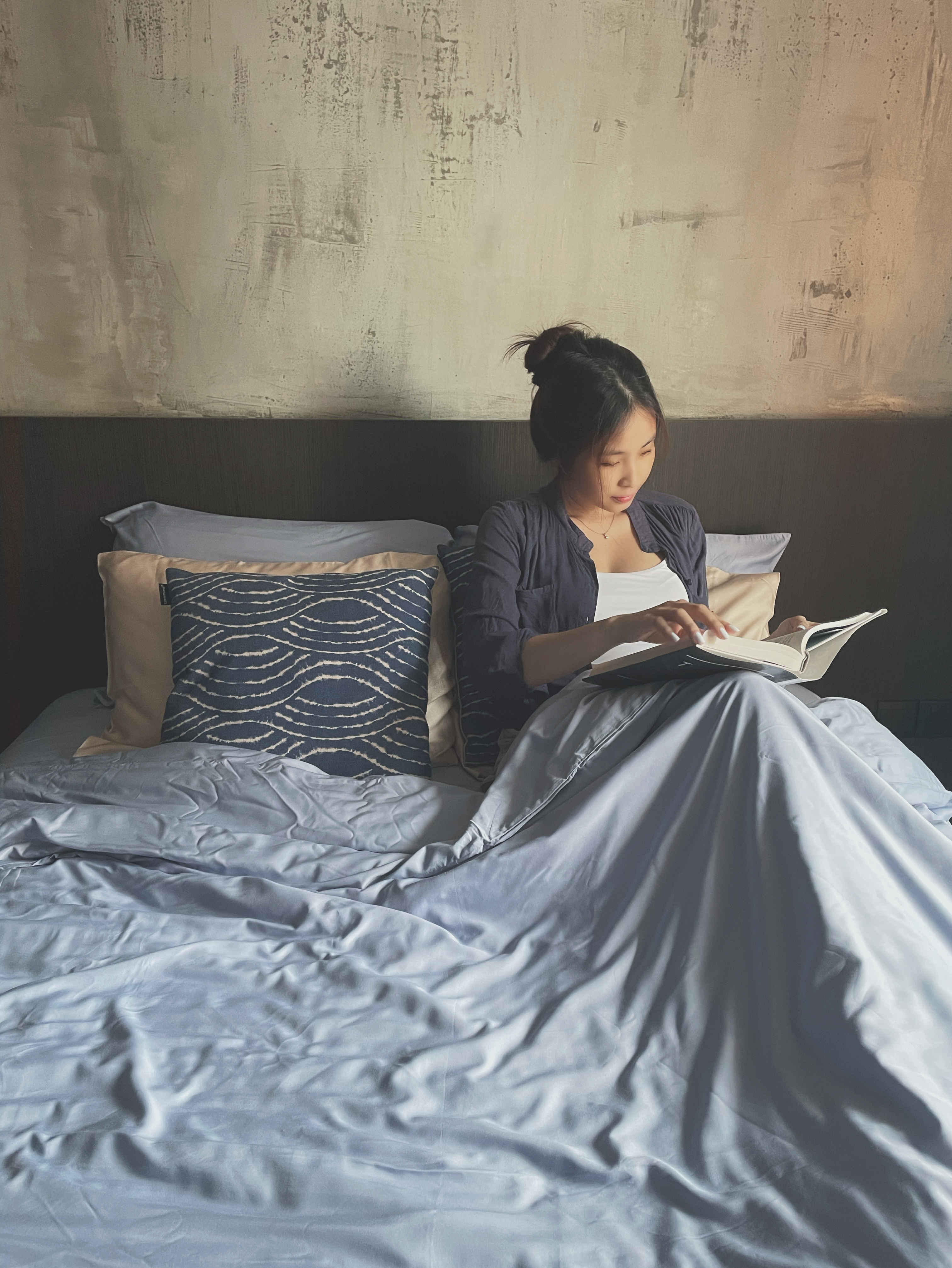 A place to rest and recharge  - Sleek modern bedroom, cozy reading nook, woman reading book, soft lighting, comfortable bed