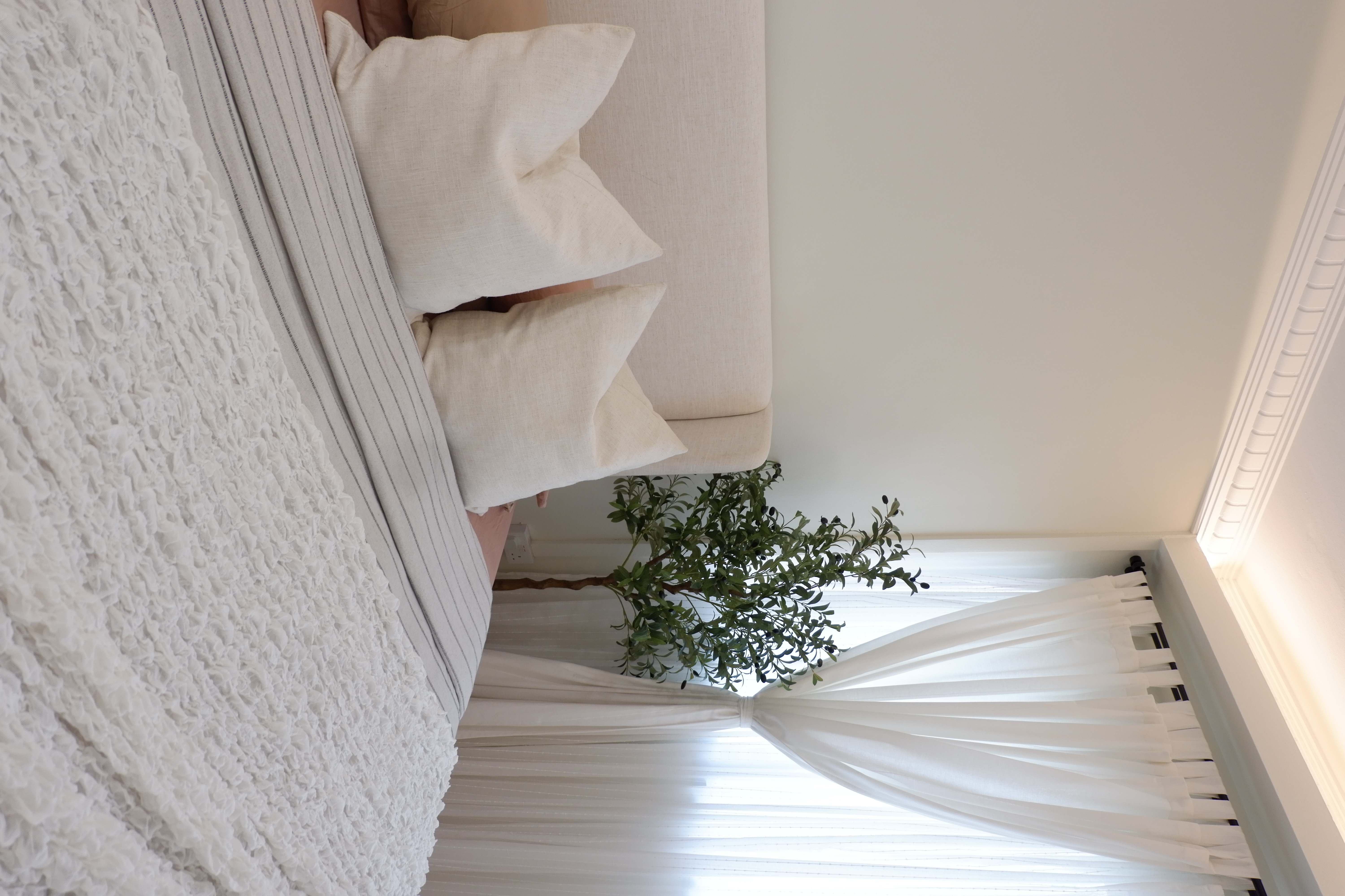 Warm and Bright Bedroom Retreat - White textured wall, beige sofa, fluffy throw blanket, elegant curtains, indoor plant