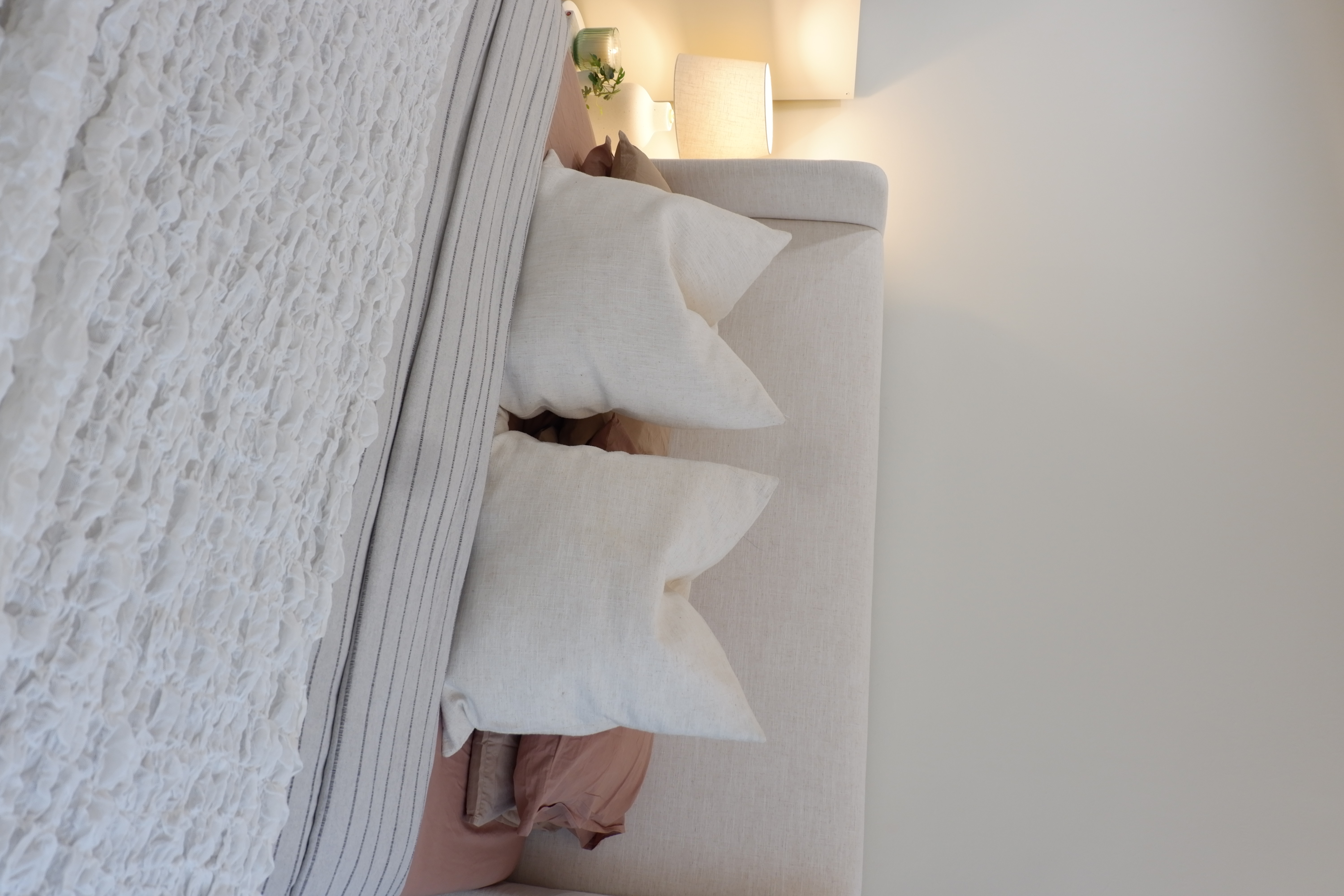 Warm and Bright Bedroom Retreat - White textured wall, cozy seating area, soft lighting, modern decor, light-colored pillows