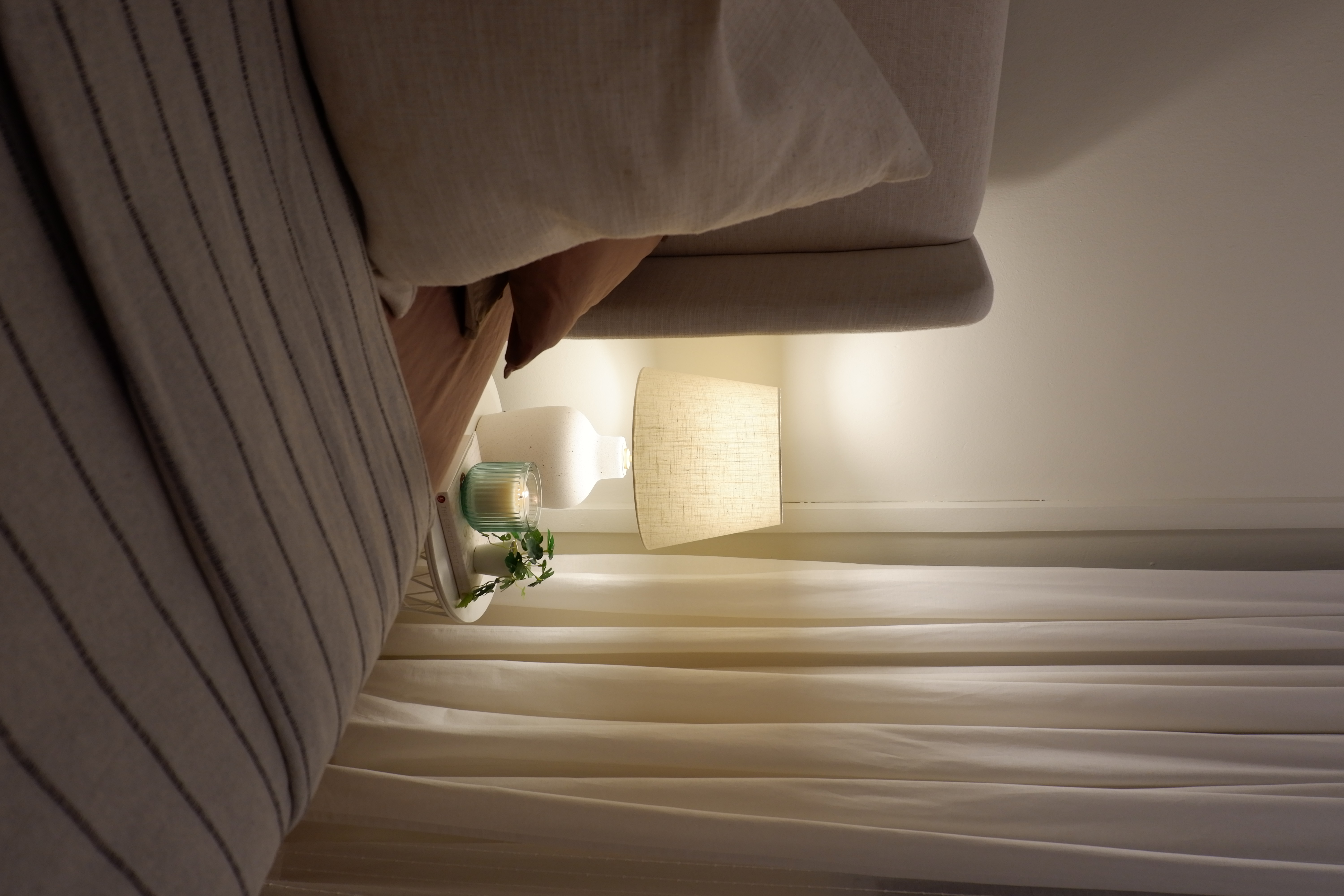 Warm and Bright Bedroom Retreat - Soft, beige striped sofa, cozy bed, warm lighting, light beige curtains, wooden headboard