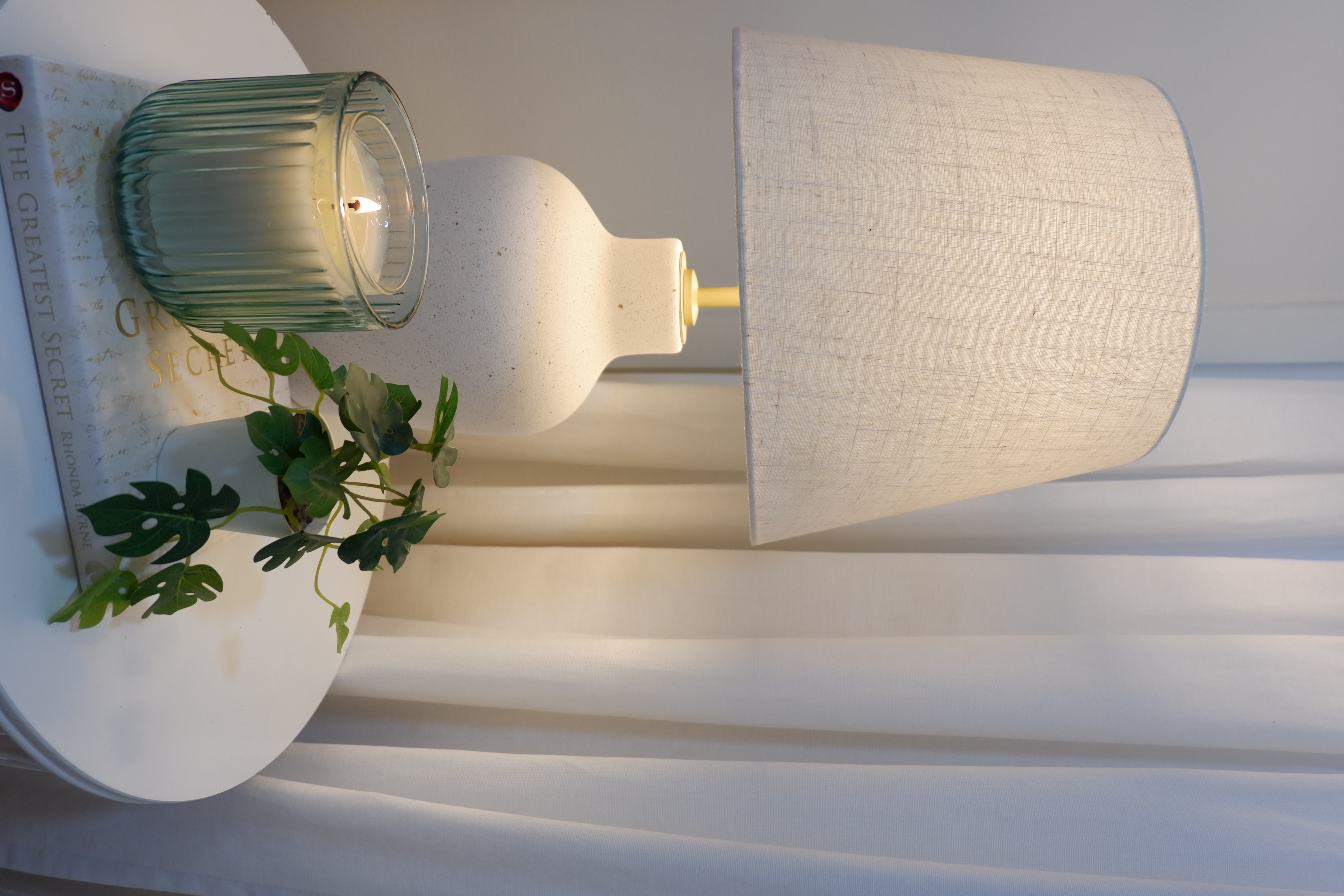 Warm and Bright Bedroom Retreat - glass candle, white lamp, indoor setting, modern decor, soft lighting, plant, white table