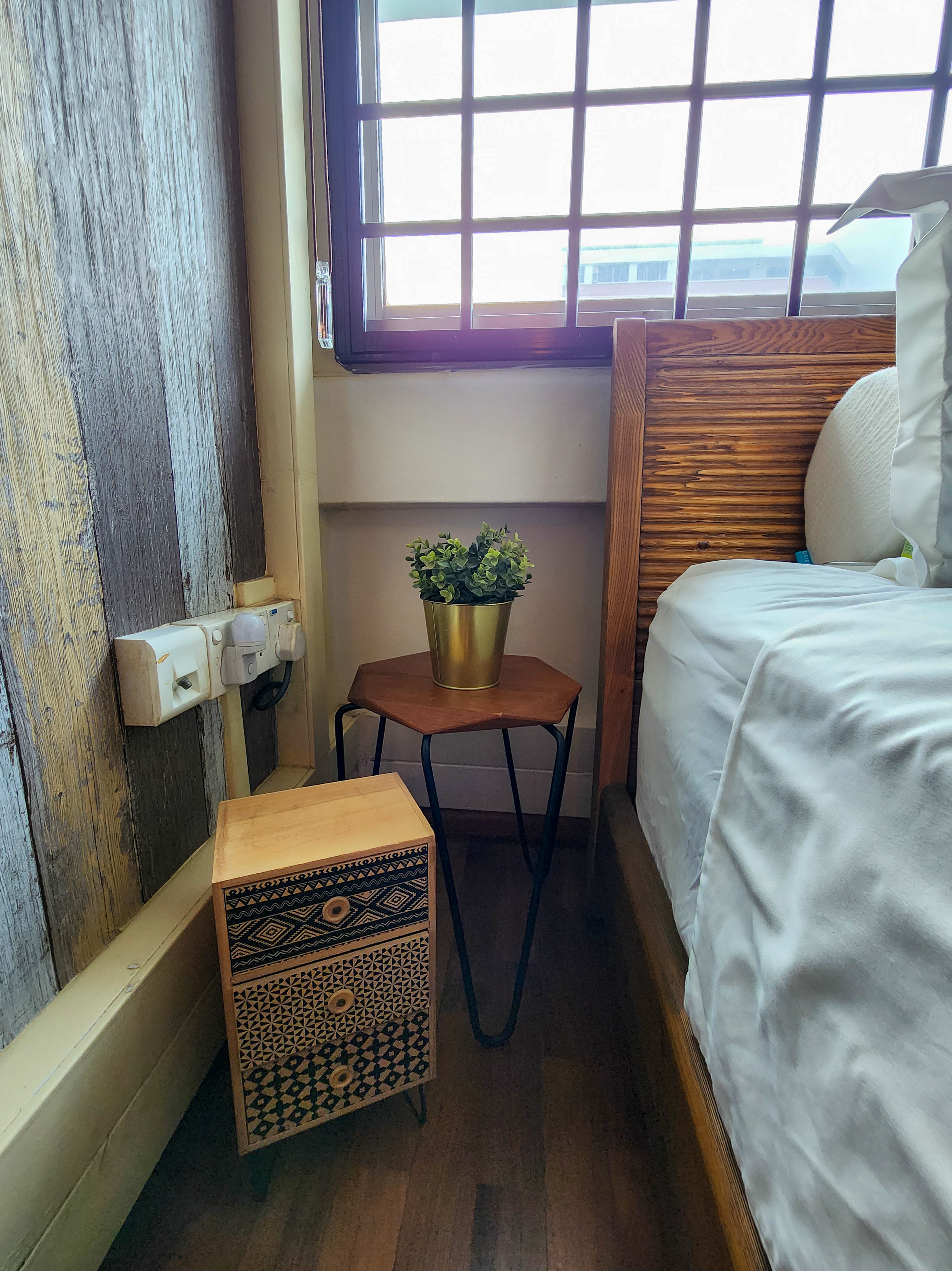 Cosy Escapade - Wooden nightstand, patterned box, small wooden stool, white bed, wooden headboard, white sheets, wooden